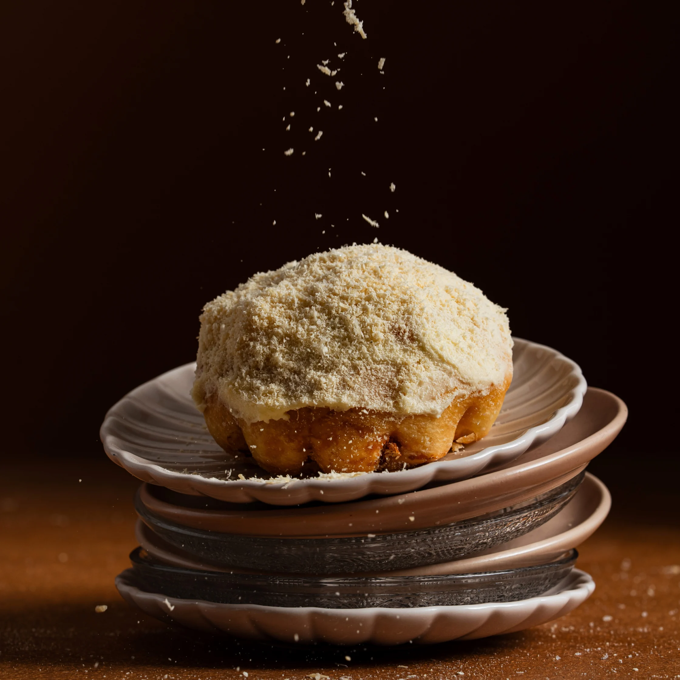 Filipino ensaymada pastry topped with grated cheese on stacked ceramic plates against a dark background.