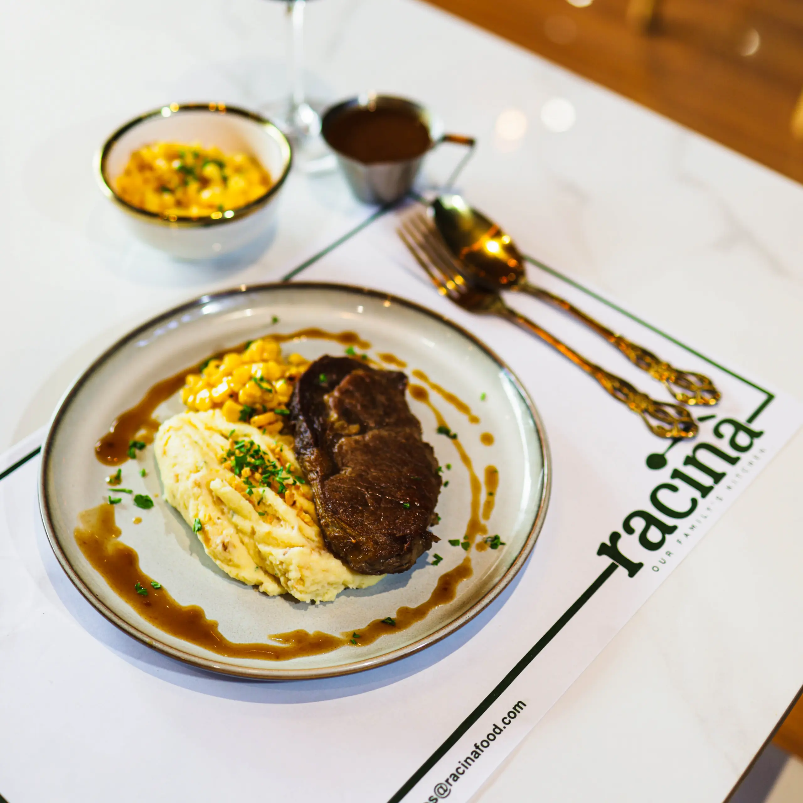 Plate with beef, mashed potatoes, and gravy on a round dish, with gold-tone cutlery nearby on a white tablecloth.