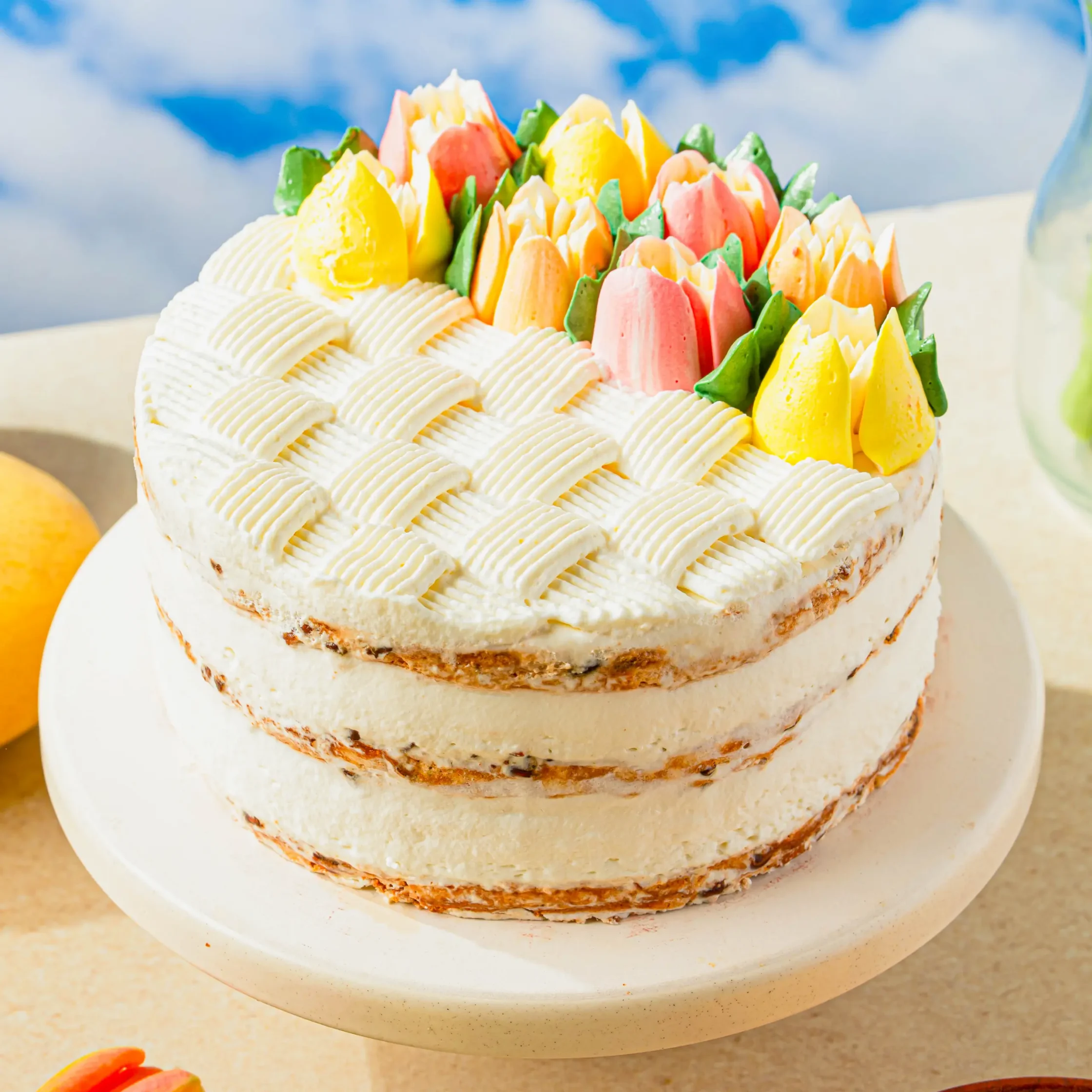 Layered white cake with piped ridged frosting and colorful buttercream flowers on top (pink, yellow, green).