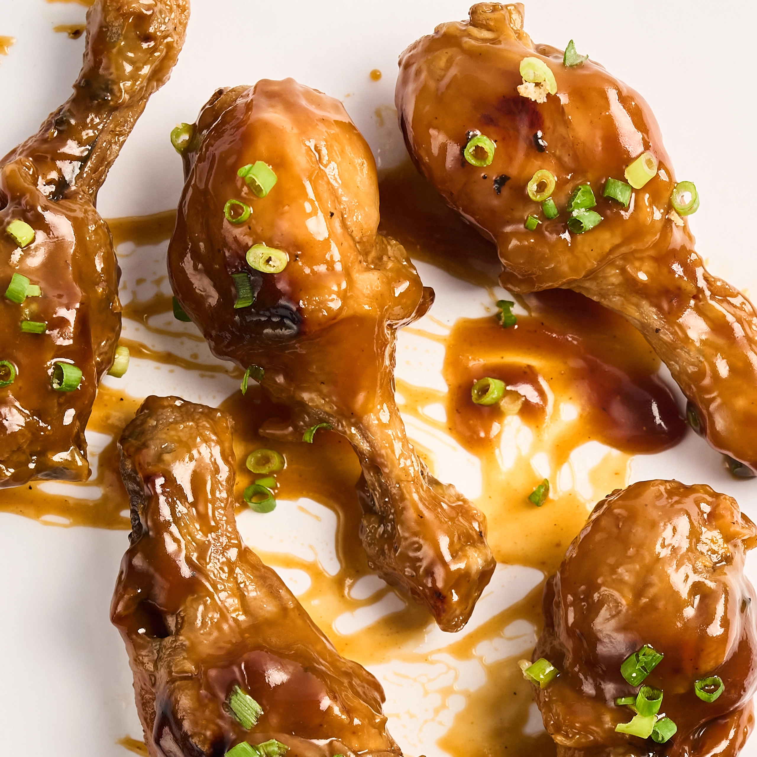 Glazed chicken wings on a plate, sprinkled with chopped green onions.