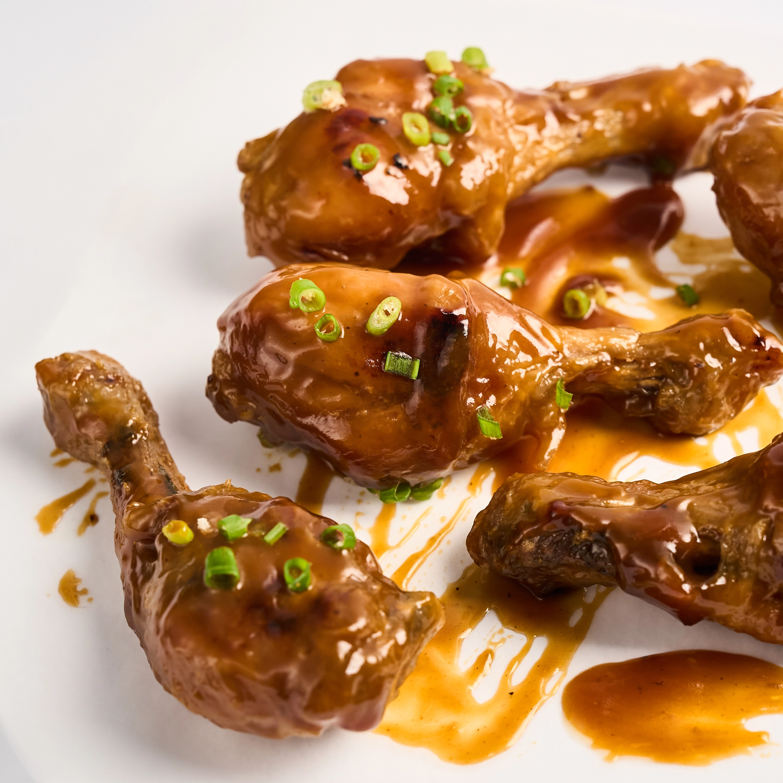 Glazed chicken wings with green onion garnish on a white plate, close-up view.