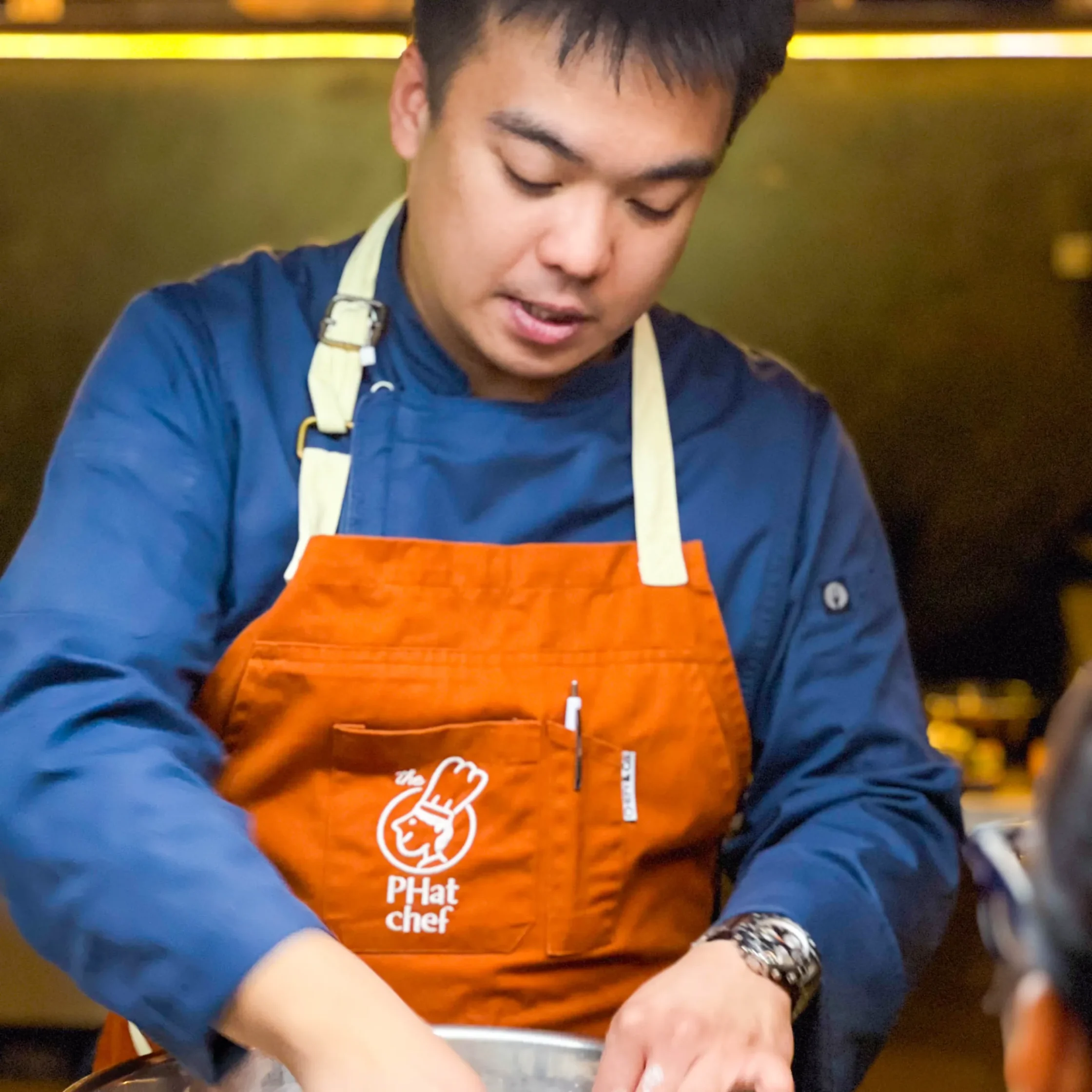 Private chef in branded apron preparing handcrafted cuisine during an upscale personal chef dining experience in a contemporary kitchen.