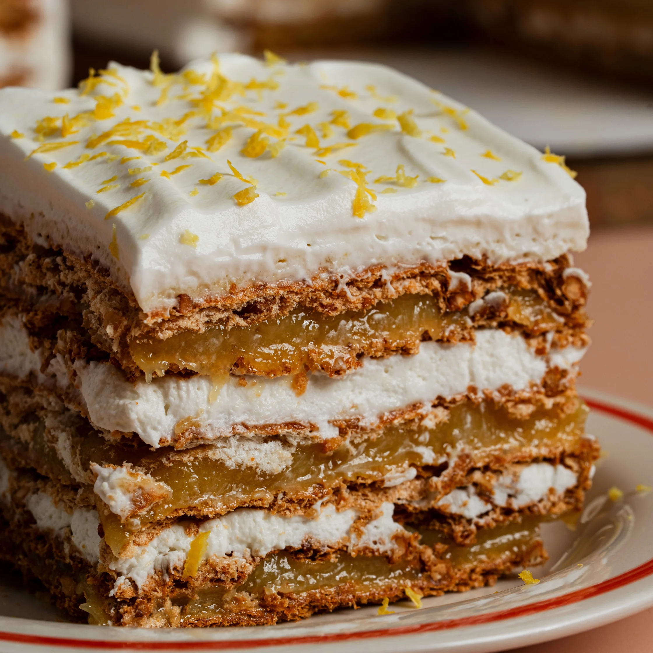 Slice of Sans Rival cake with layered buttercream and cashew meringue topped with whipped cream and lemon zest.