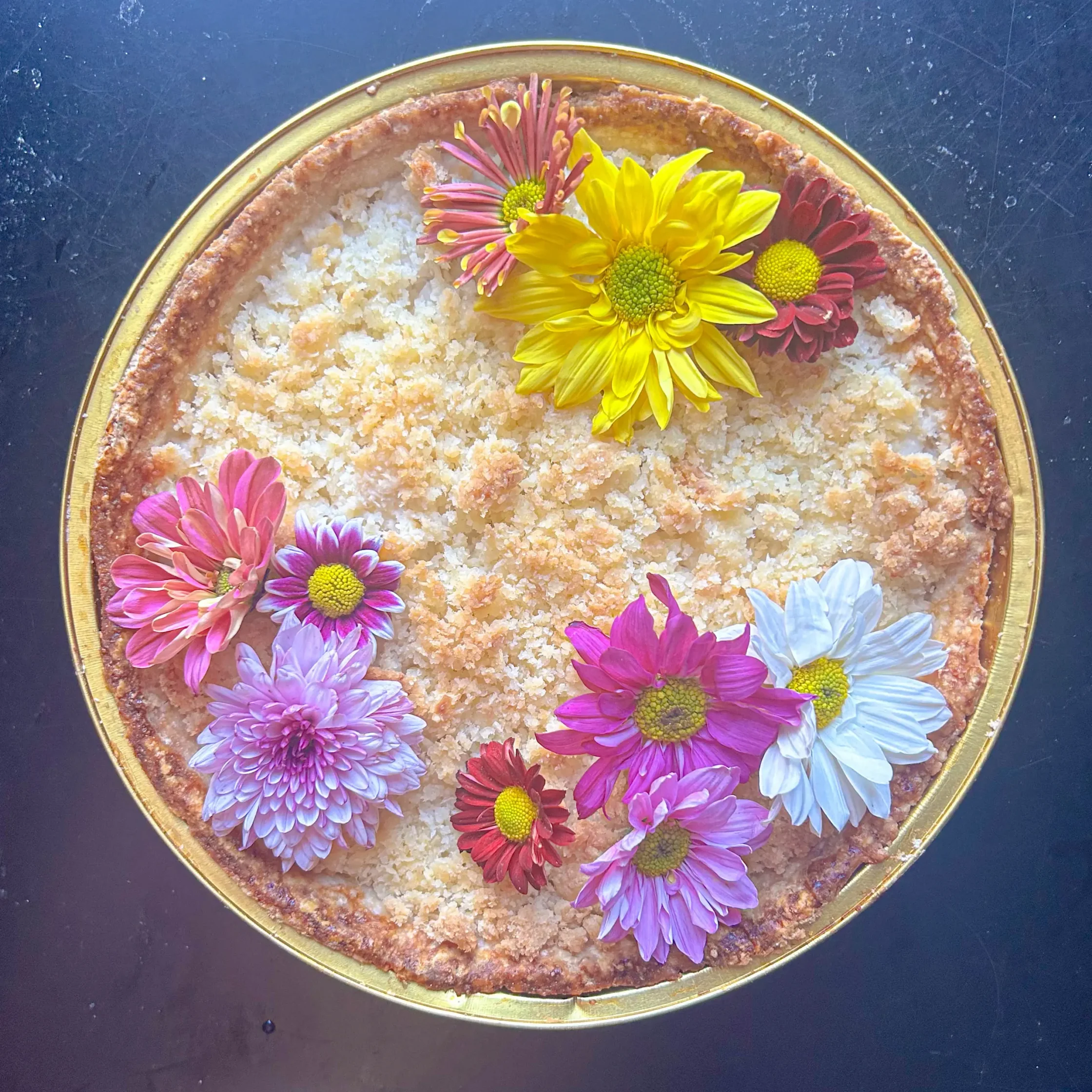 Round tart topped with colorful flowers and flaky salt, set on a dark surface.
