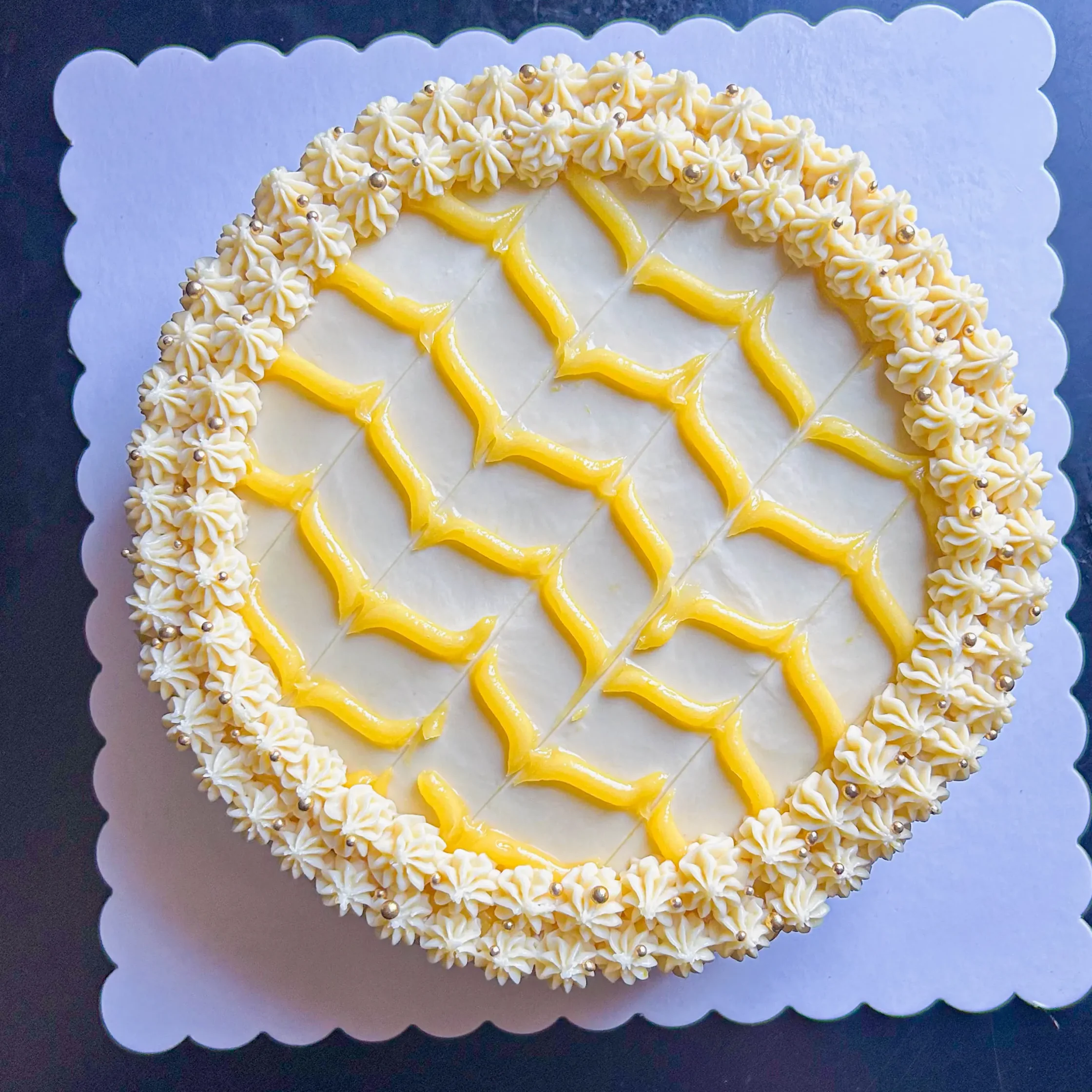 Round cake with white rosettes around the edge and yellow icing accents on a scalloped display board