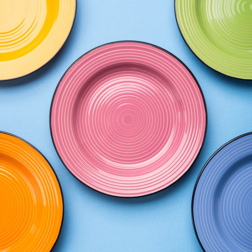 Collection of colorful dining plates and bowls arranged on a red background, showcasing various tableware sizes and styles used for dinner, salads, desserts, soups, and side dishes.