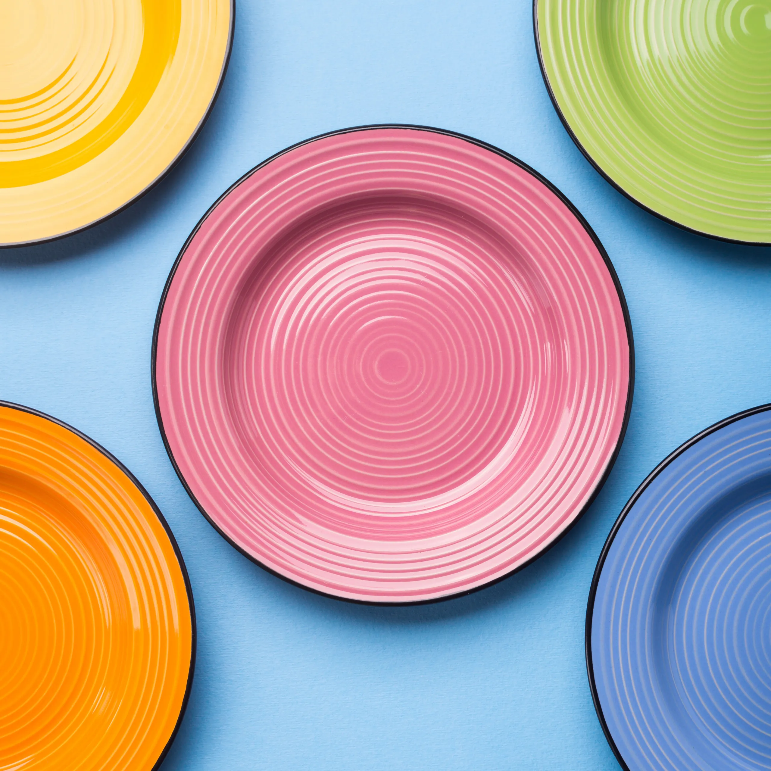 Collection of colorful dining plates and bowls arranged on a red background, showcasing various tableware sizes and styles used for dinner, salads, desserts, soups, and side dishes.