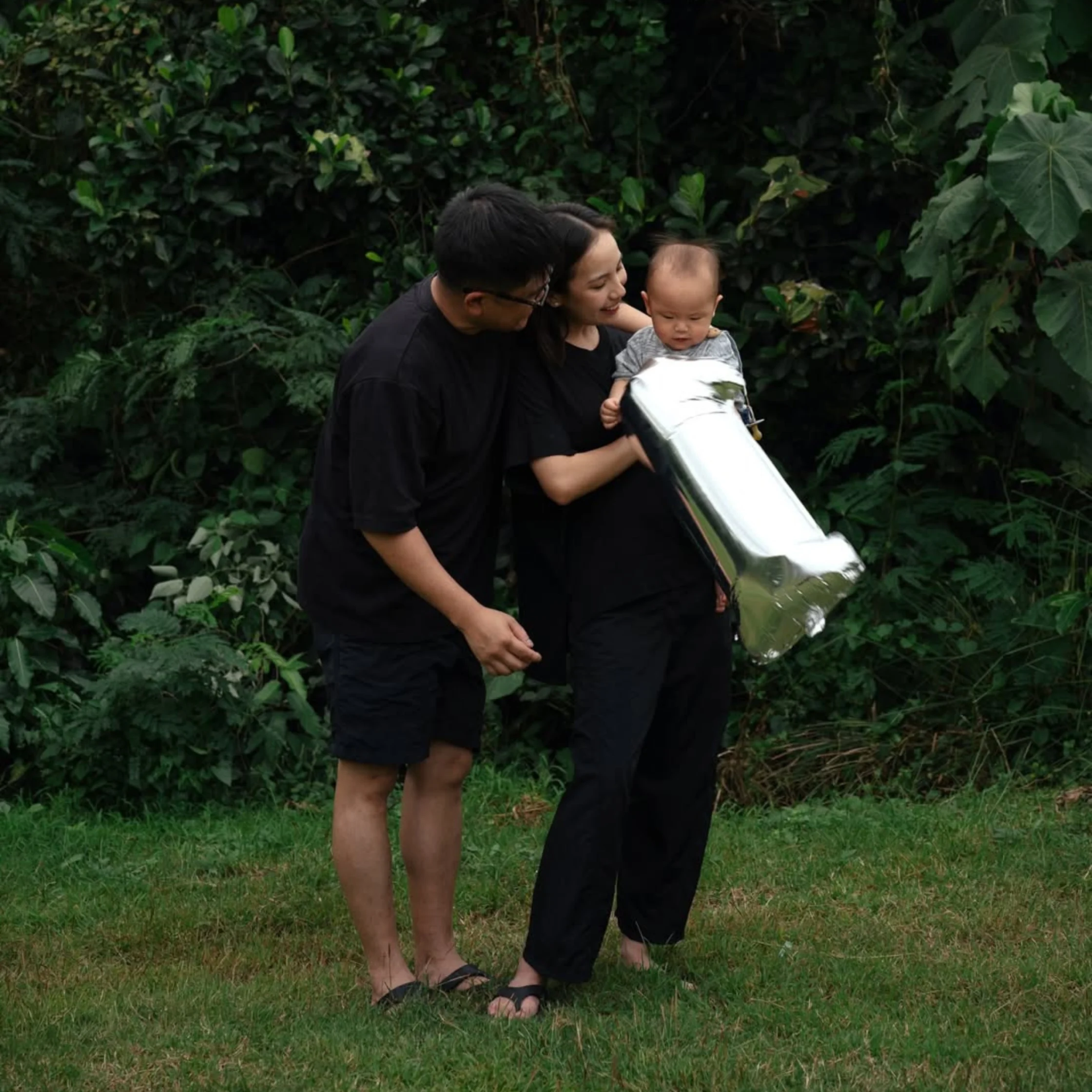 Bryan Kong, Maxine Kong and baby Magnus enjoying family time outdoors in a garden, relaxed lifestyle photo with natural greenery backdrop