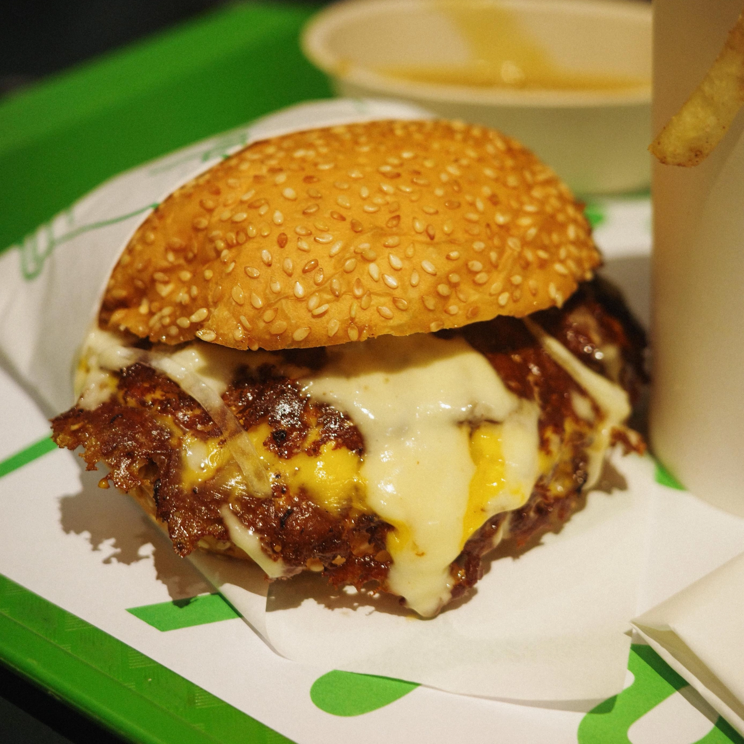 Close-up of a sesame-seed burger bun with melted cheese and beef patty showing through.