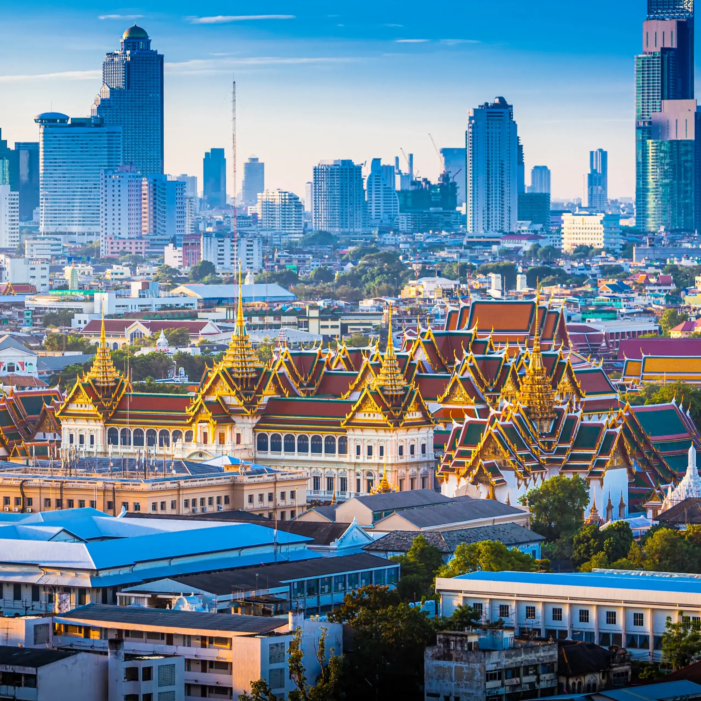 City skyline with modern skyscrapers behind a golden Thai temple in the foreground against a blue sky.