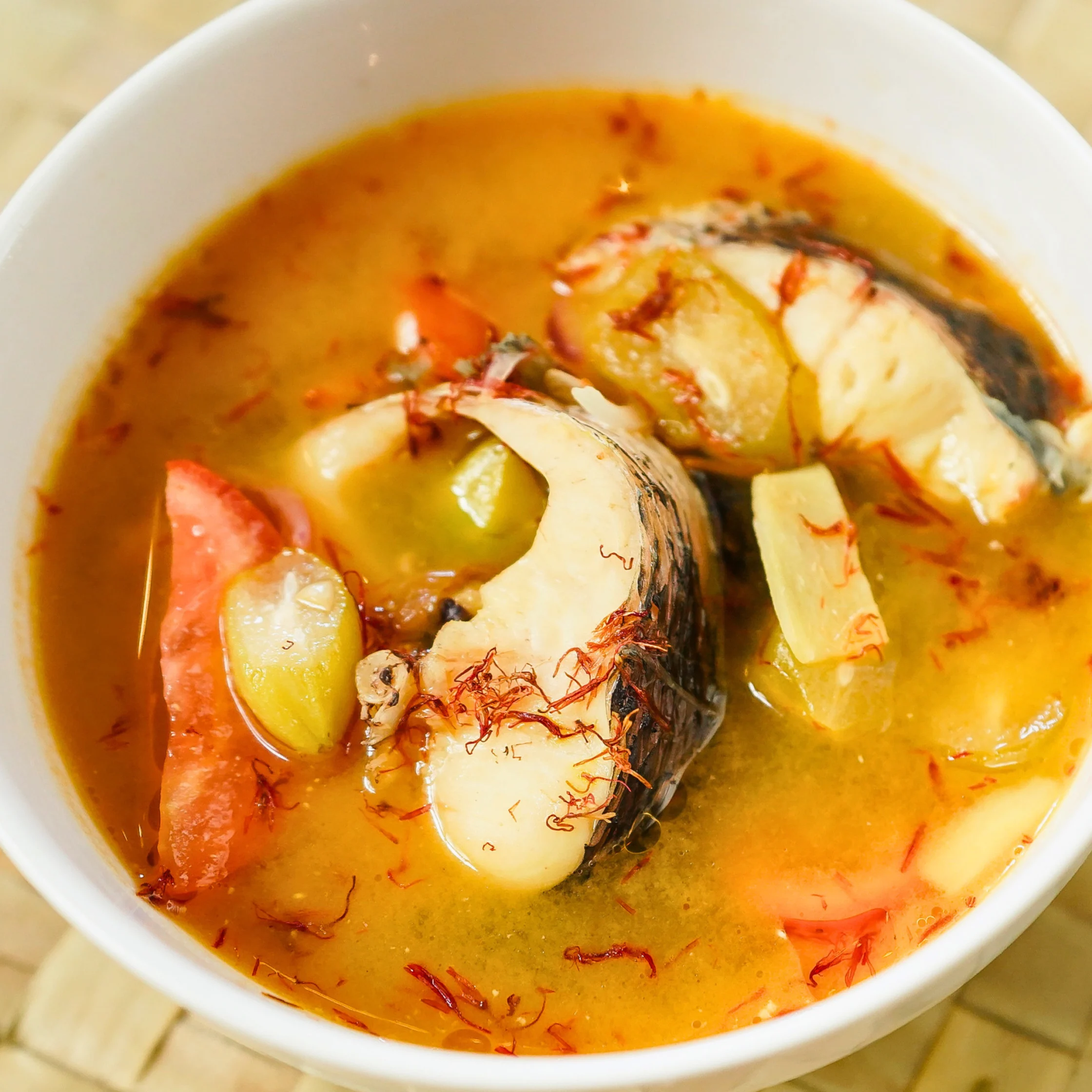 Bowl of Cachuelang Isda, a yellow-tinted sour fish soup with fish steaks, vegetables, and kasubha threads in a rich broth.
