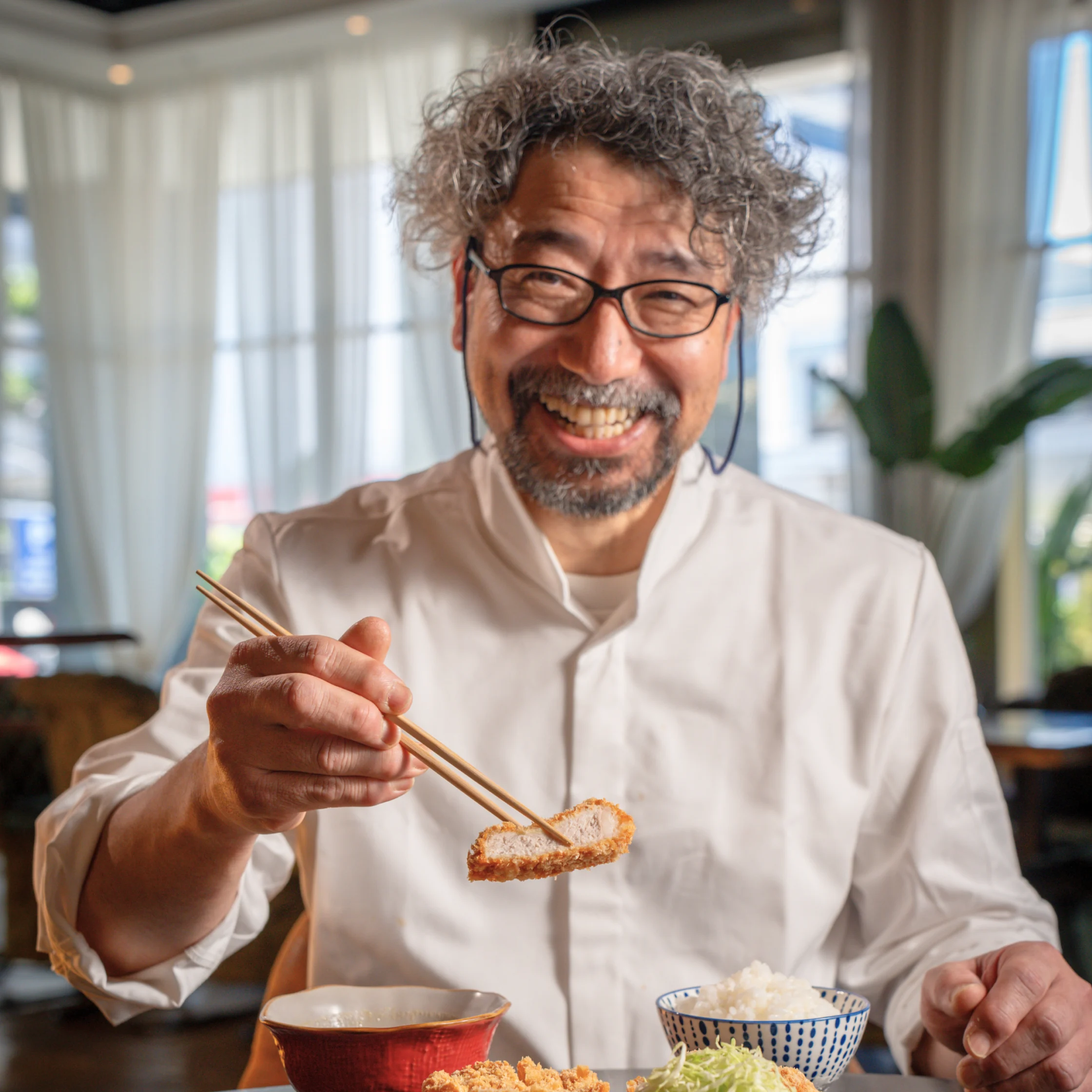 Chef Hironobu Horiuchi holds a piece of crispy tonkatsu with chopsticks, showcasing the dish that earned Tonkatsu Horiichi Michelin Bib Gourmand recognition.