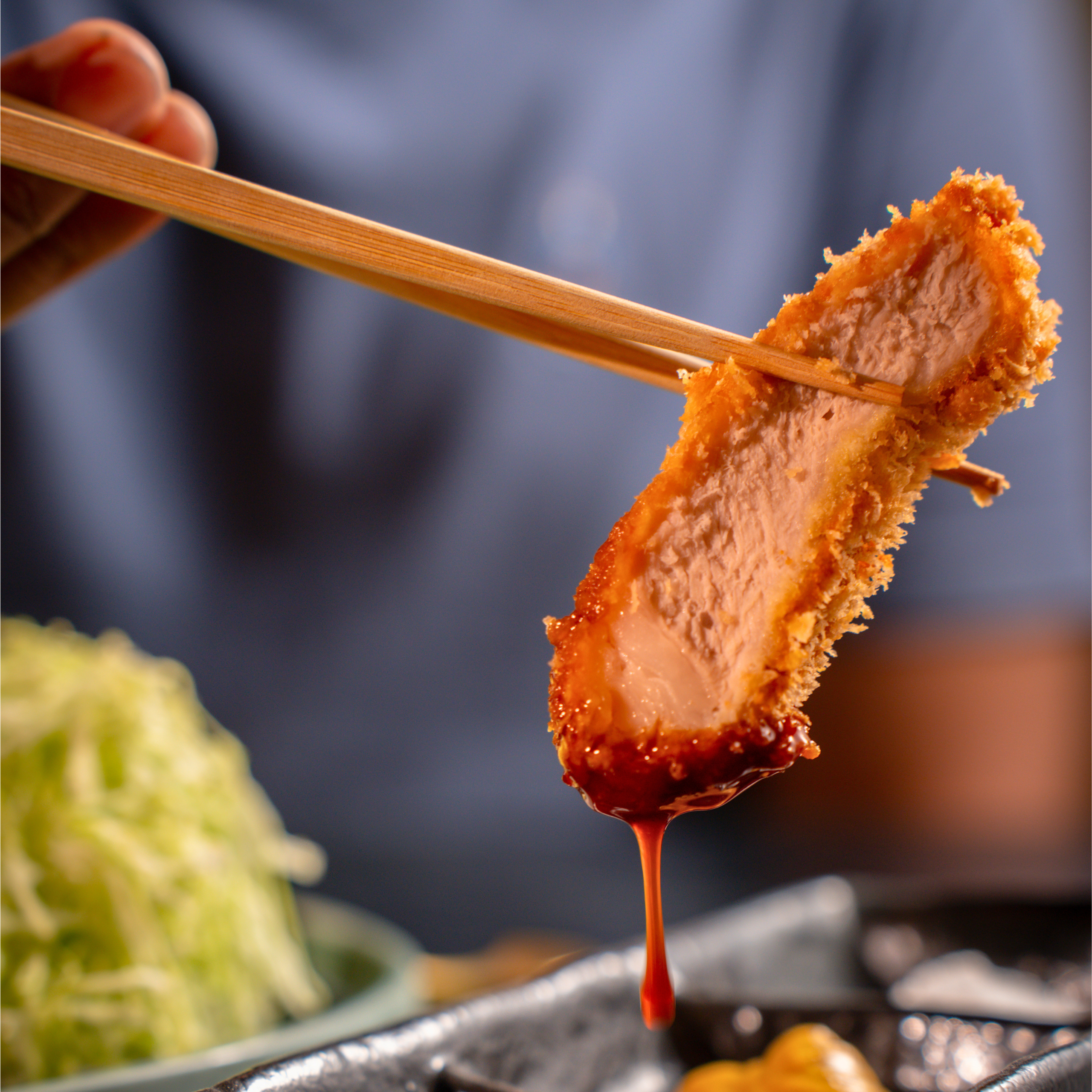 A slice of golden-brown tonkatsu dipped in sauce, highlighting the juicy interior and delicate crust achieved through Chef Hironobu Horiuchi's double-frying technique.