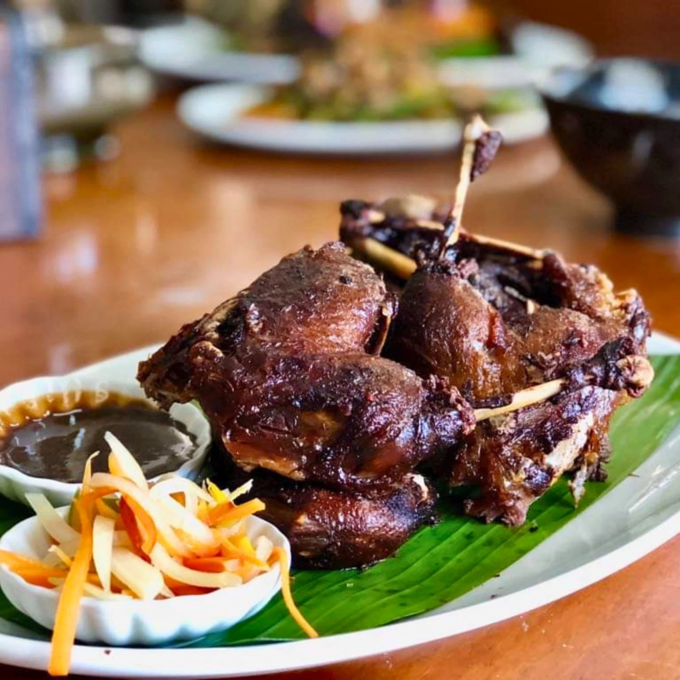Plate of Kinulob na Itik, braised then fried duck with crisp dark skin, served with pickled vegetables and dipping sauce.