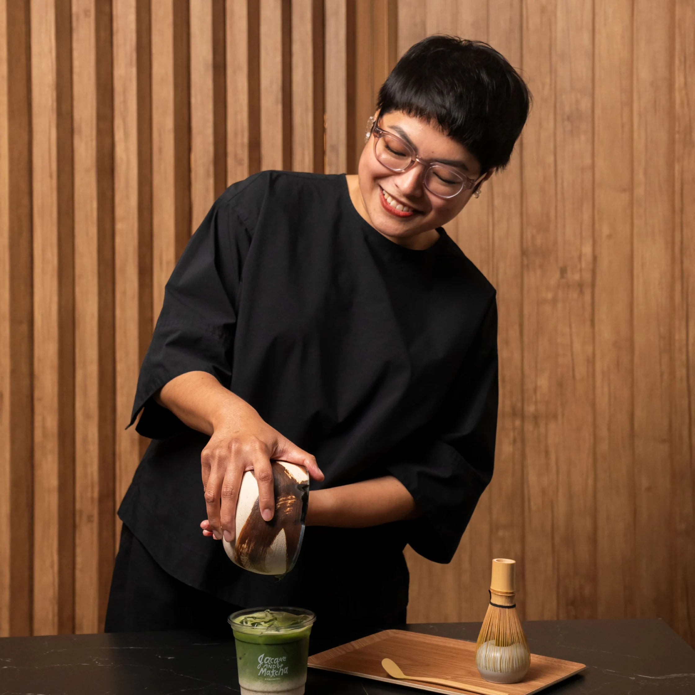 Jacque de Borja-Medestomas uses a bamboo whisk to blend matcha in a ceramic bowl during a traditional tea preparation process.