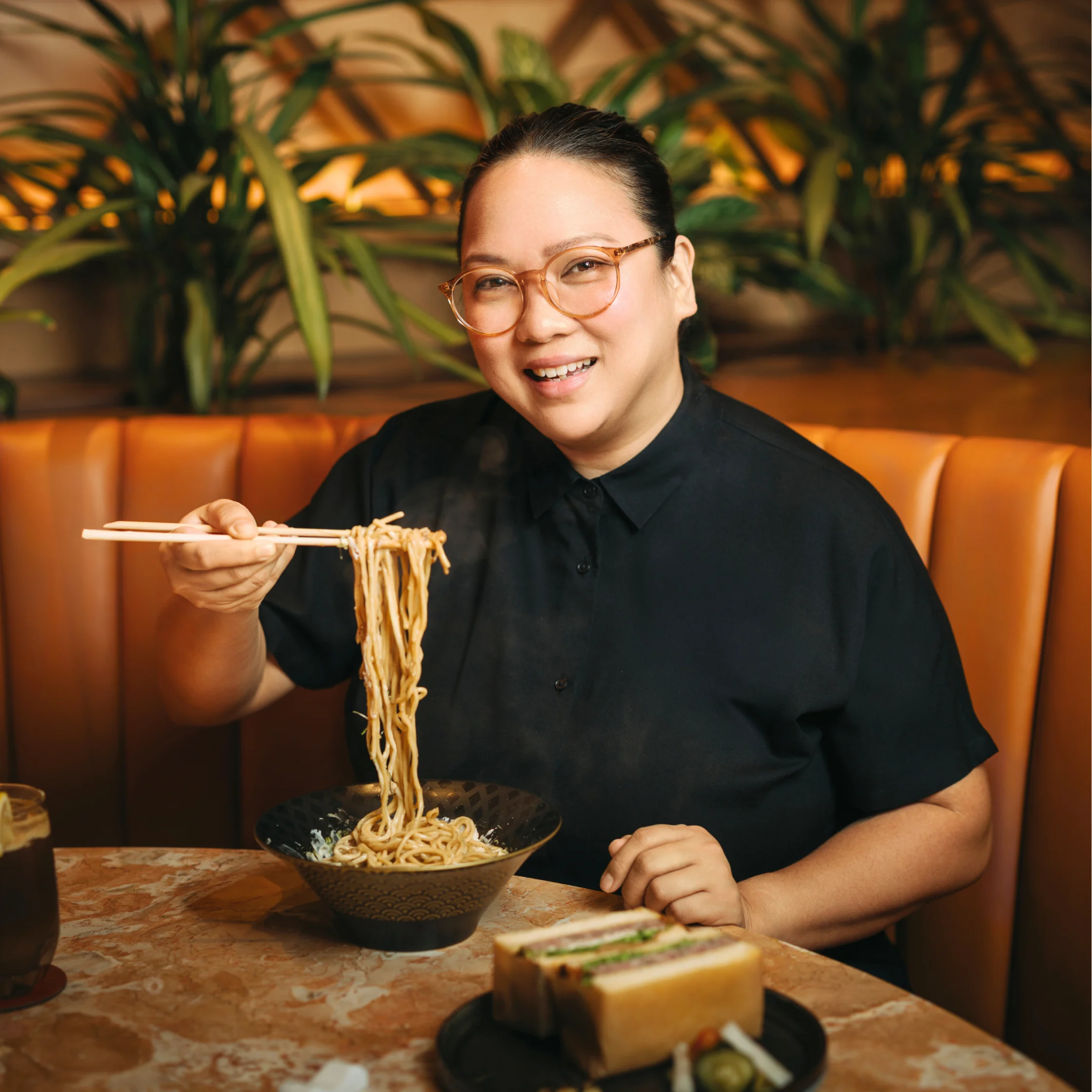 Portrait of Miko Calo in a restaurant dining area, standing and smiling in a warmly lit interior.