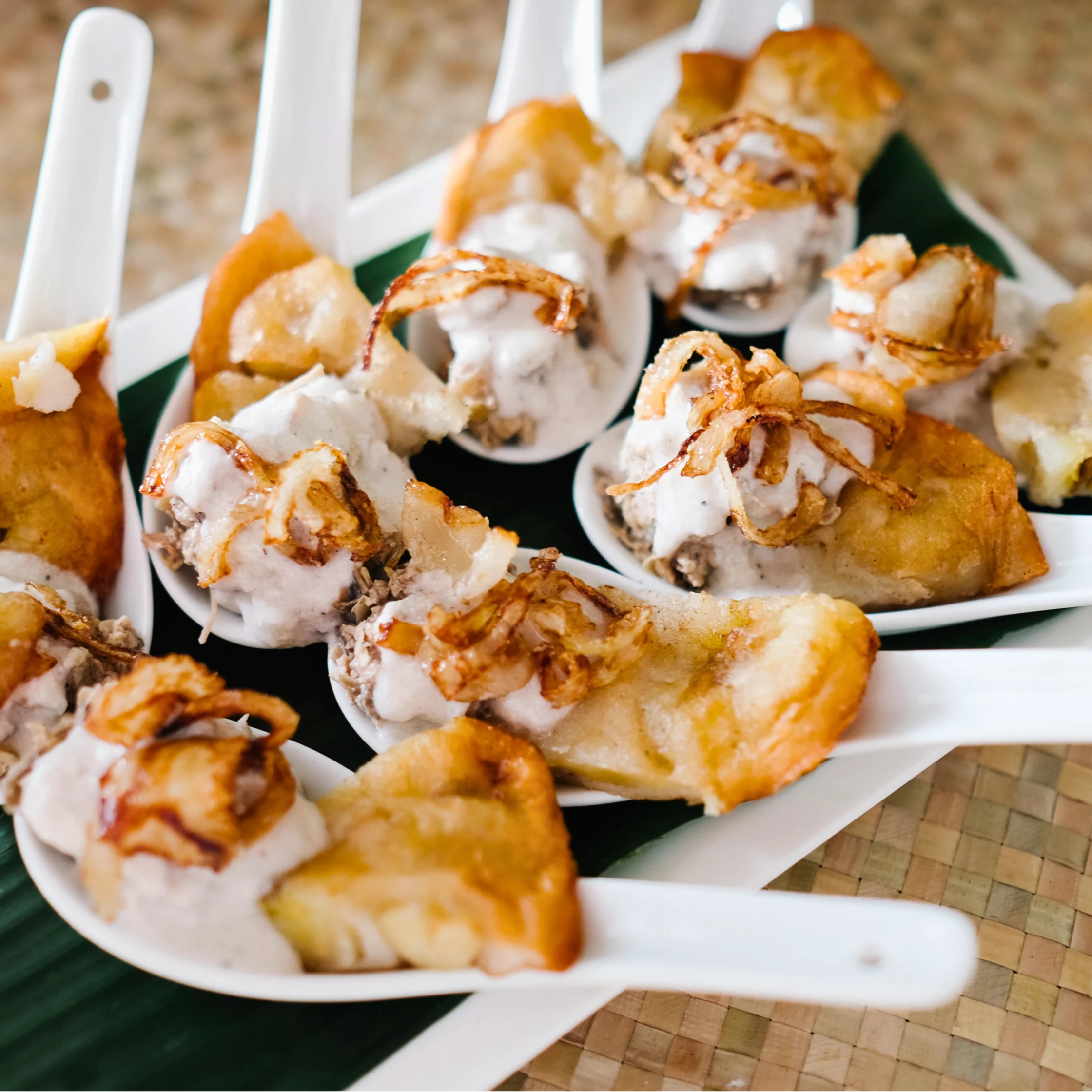 Minanok appetizer served on tasting spoons, featuring shredded banana blossom cooked in burnt coconut, topped with coconut sauce and fried onion.