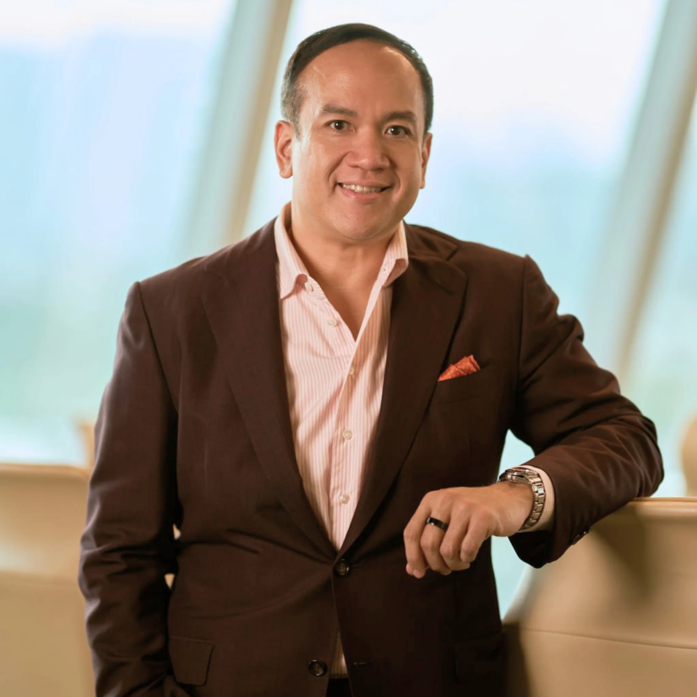 Professional portrait of Ryan Cruz standing indoors in business attire, smiling at the camera.