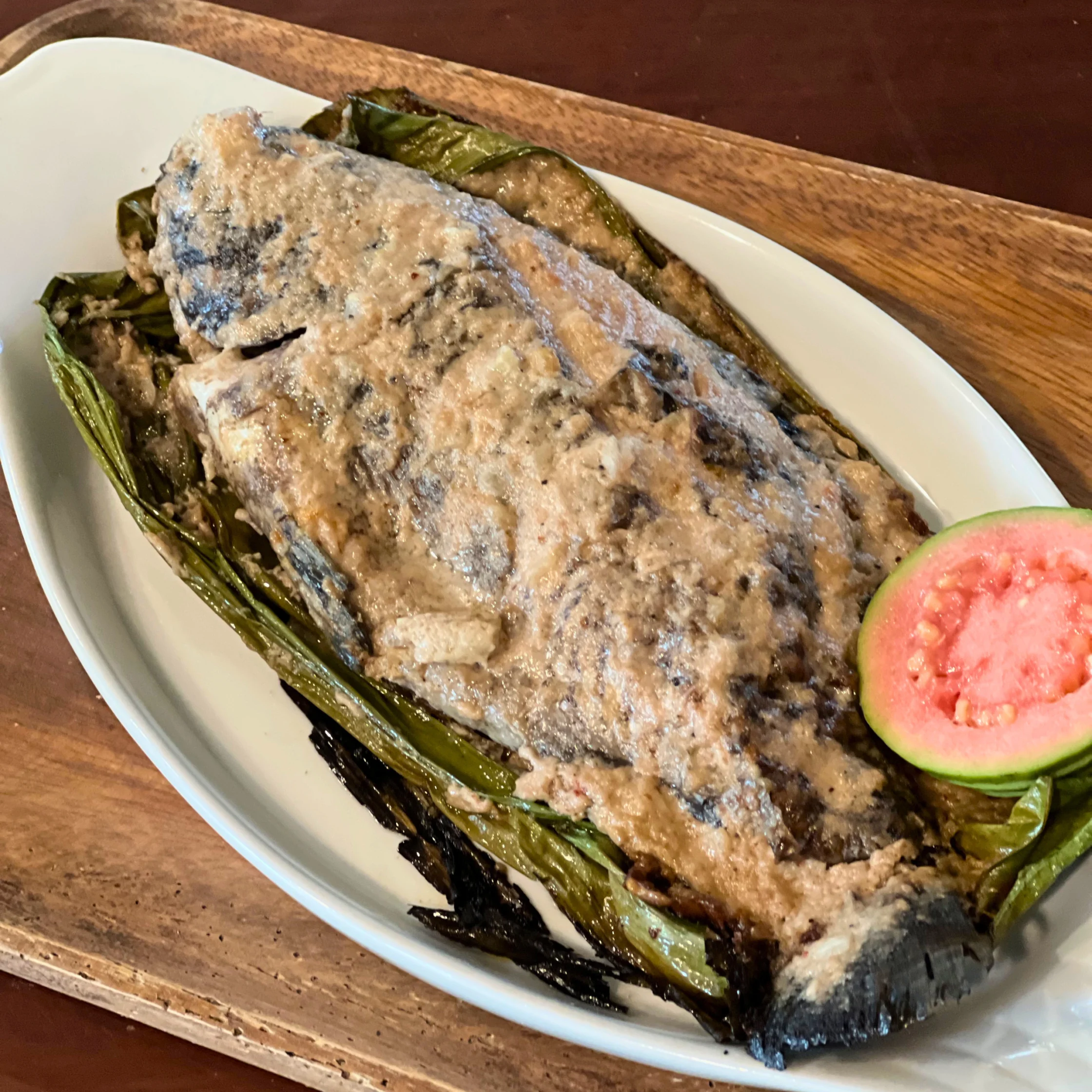 Whole Sinugnong Tilapia grilled on banana leaves and coated with a thick burnt coconut cream and guava glaze, served with grilled greens.