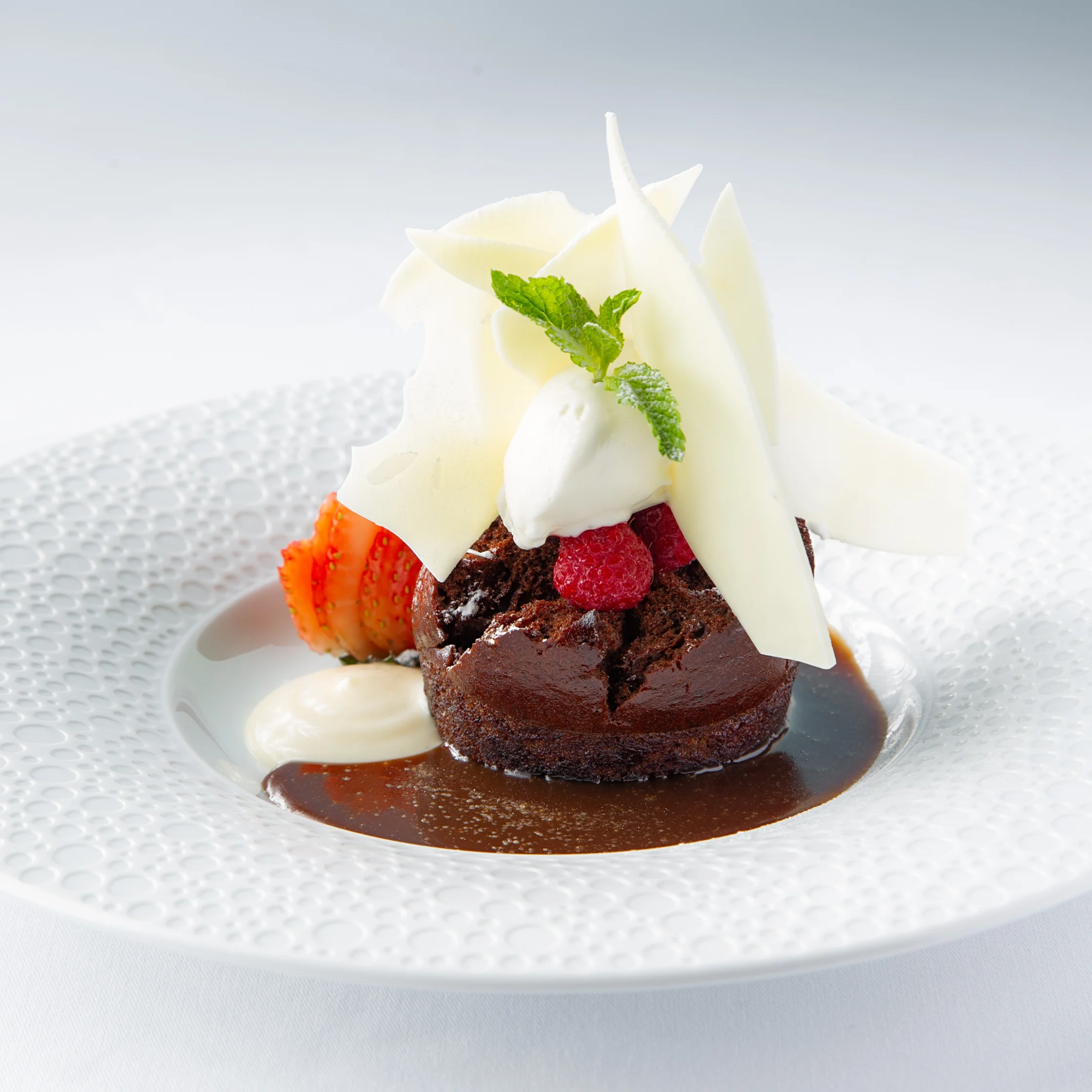 BRONTË Sticky Toffee Pudding served with toffee sauce, fresh berries, cream, and delicate white chocolate shards on a white textured plate.