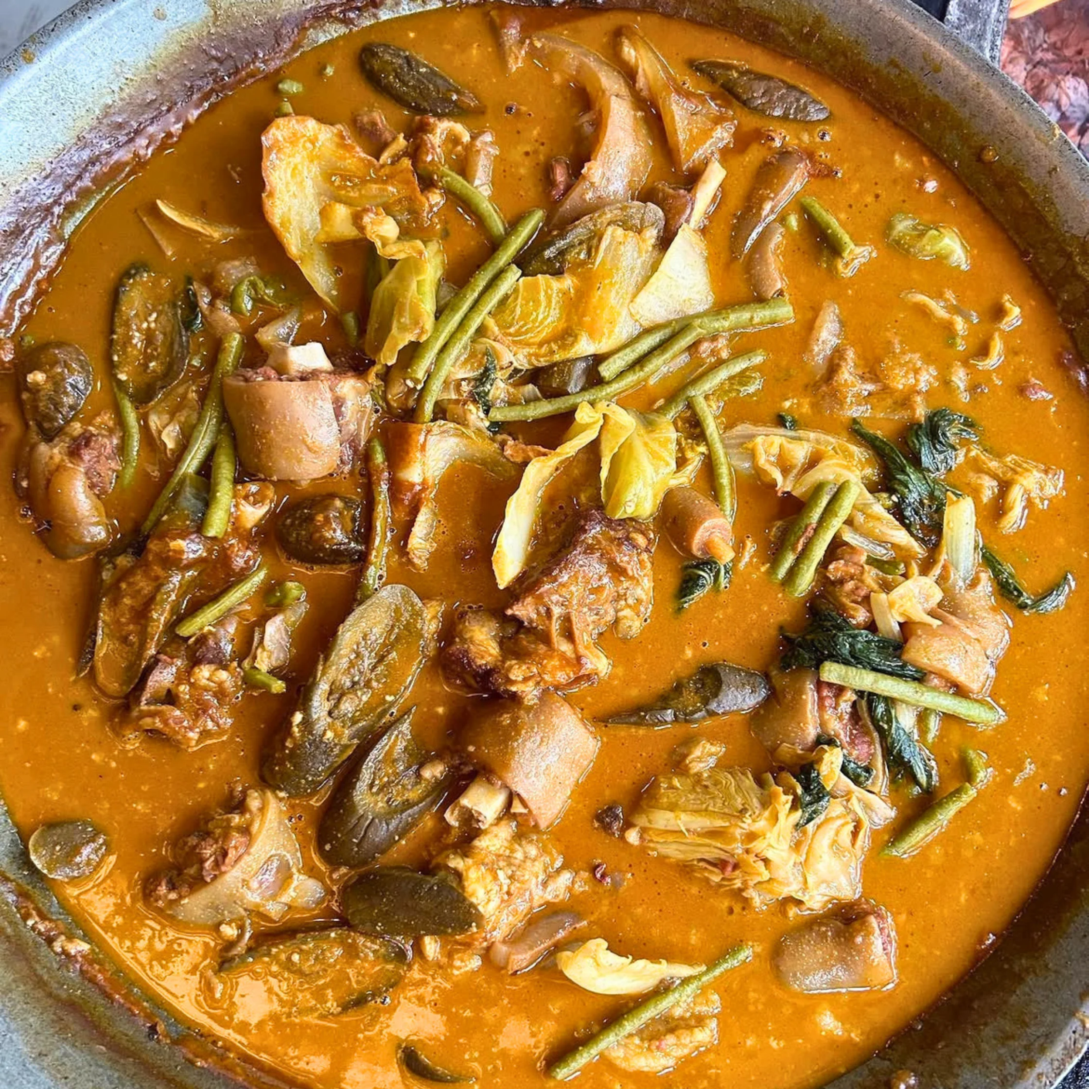 Likely Bulanglang Kapampangan or a variation of Bringhe-style vegetable stew with pork. The orange-red broth and combination of pork, talong (eggplant), sitaw (string beans), and leafy vegetables suggest a hearty Kapampangan stew. It may also be a regional vegetable-and-pork dish cooked with annatto and spices.