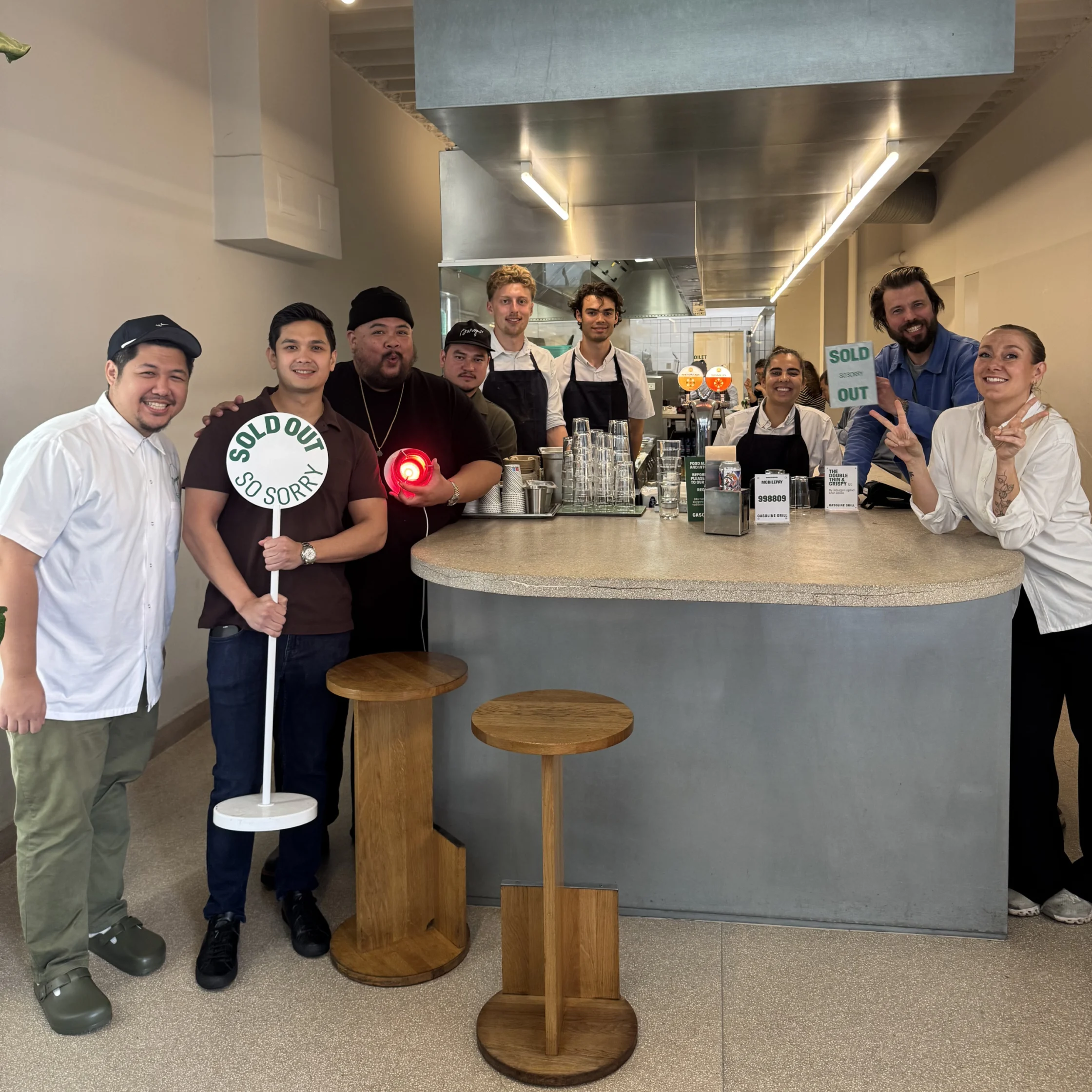 Alvin Cailan and the restaurant team pose together behind the counter while holding “Sold Out” signs after the burger pop-up event.
