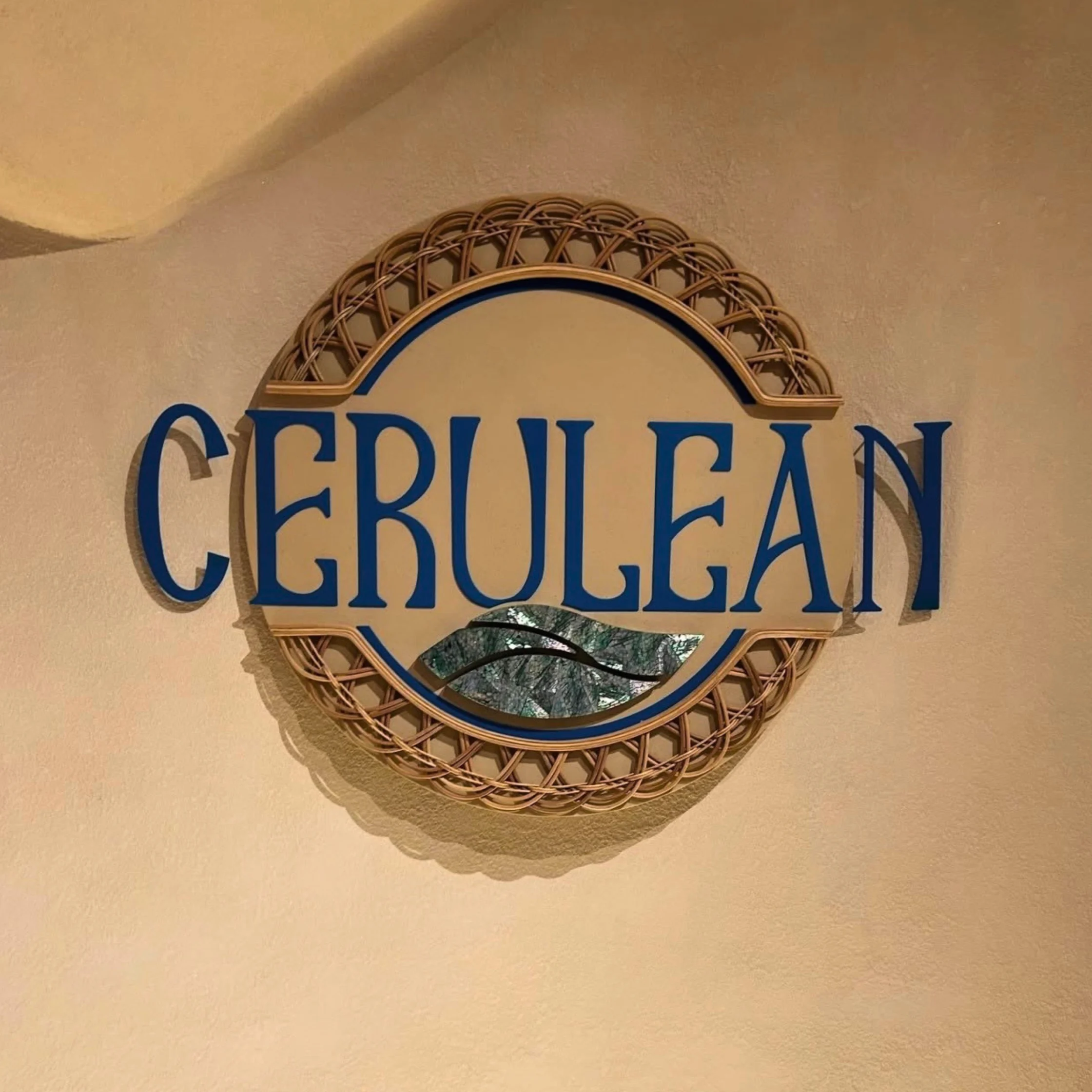 Decorative wall sign reading ‘CERULEAN’ in blue lettering, framed by a woven circular design