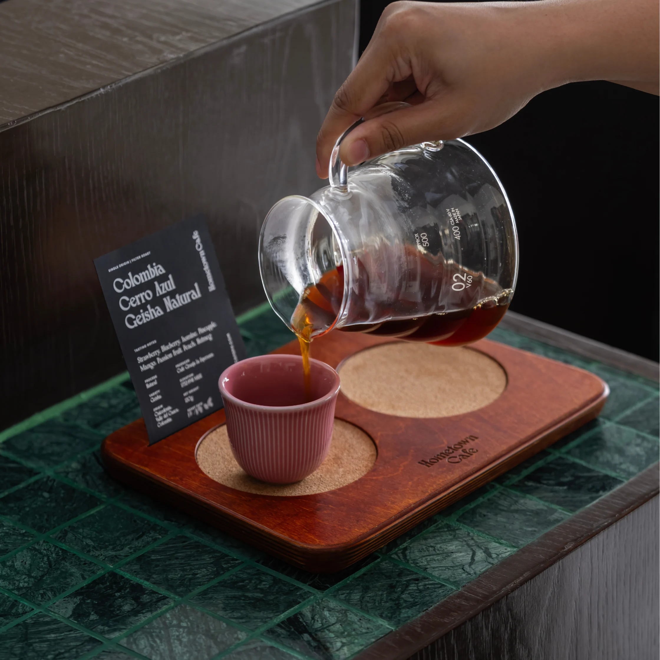 Freshly brewed coffee being poured into a ceramic cup at Hometown Cafe, served with a coffee tasting card on a wooden tray.