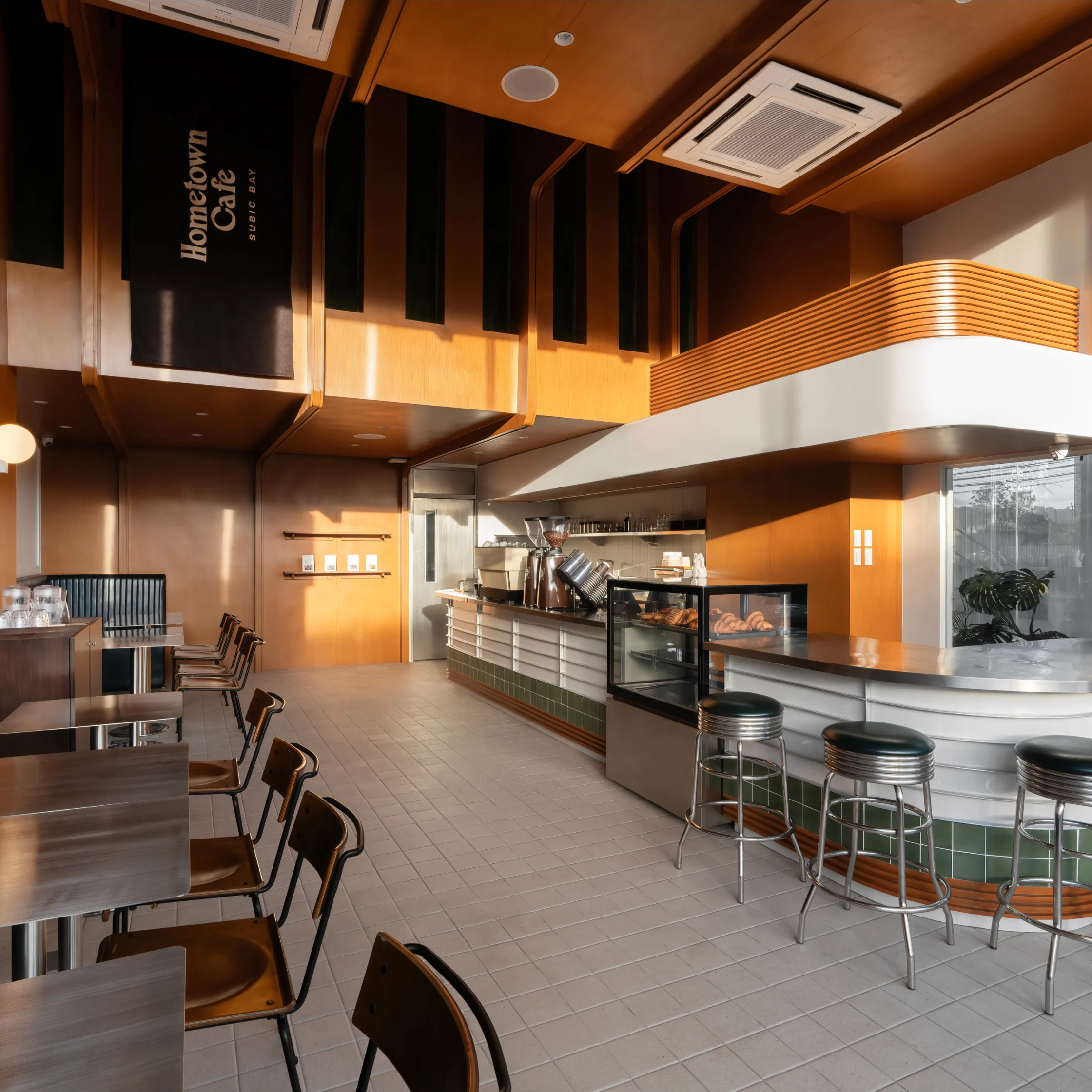 Sunlit interior of Hometown Cafe with warm wood finishes, counter seating, pastry display case, and modern retro-inspired furnishings.