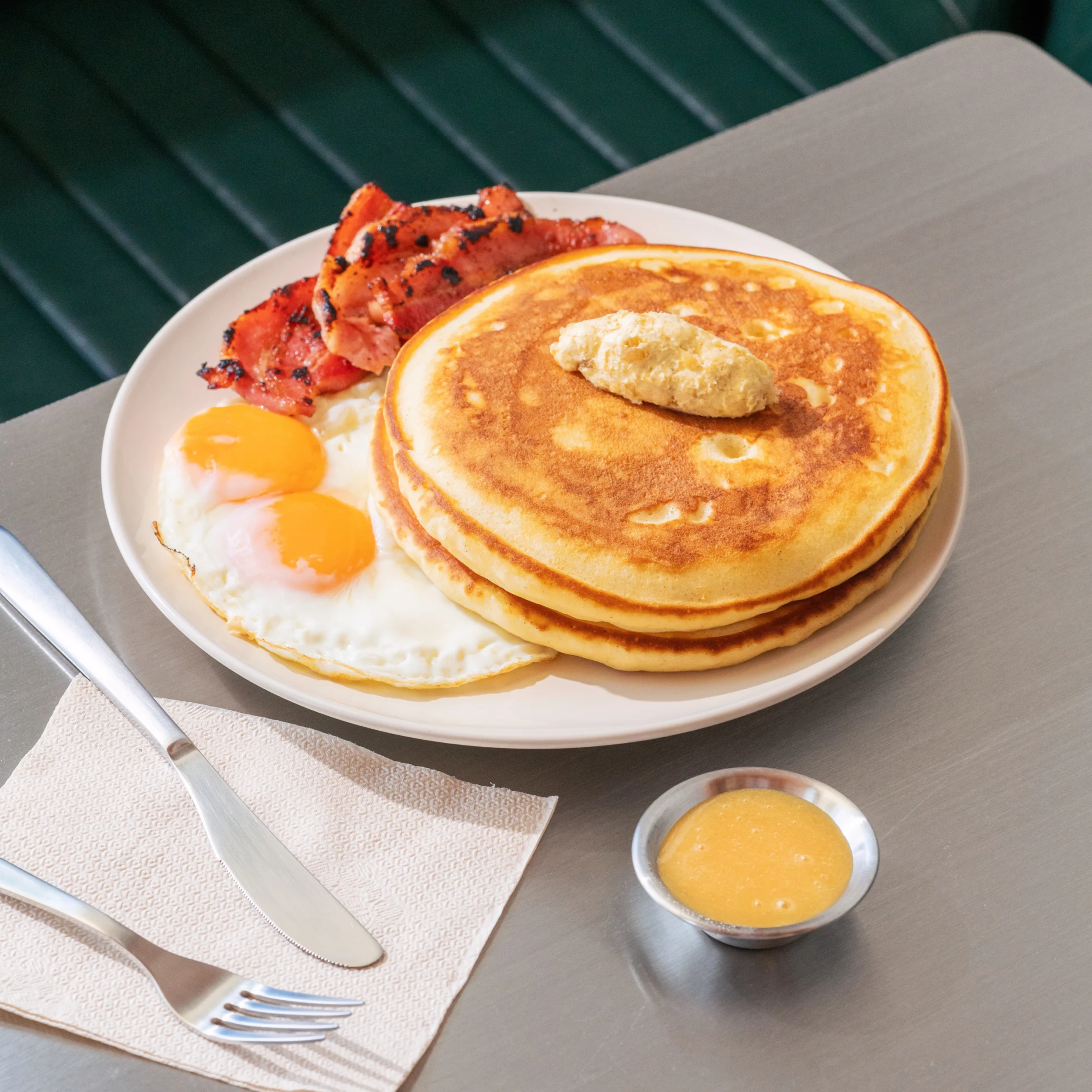 Breakfast plate at Hometown Cafe with fluffy pancakes, sunny-side-up eggs, grilled bacon, butter, and a side of syrup.