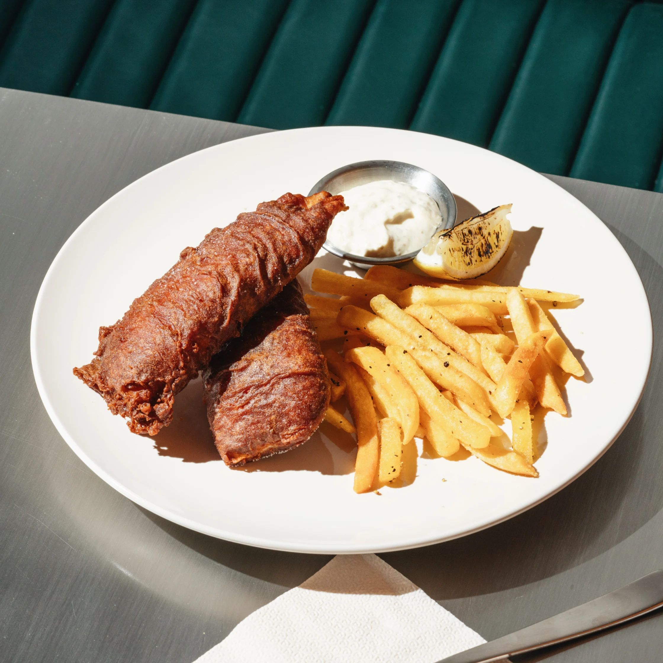 Hometown Cafe fish and chips featuring crispy battered fish, golden fries, tartar sauce, and a grilled lemon wedge.