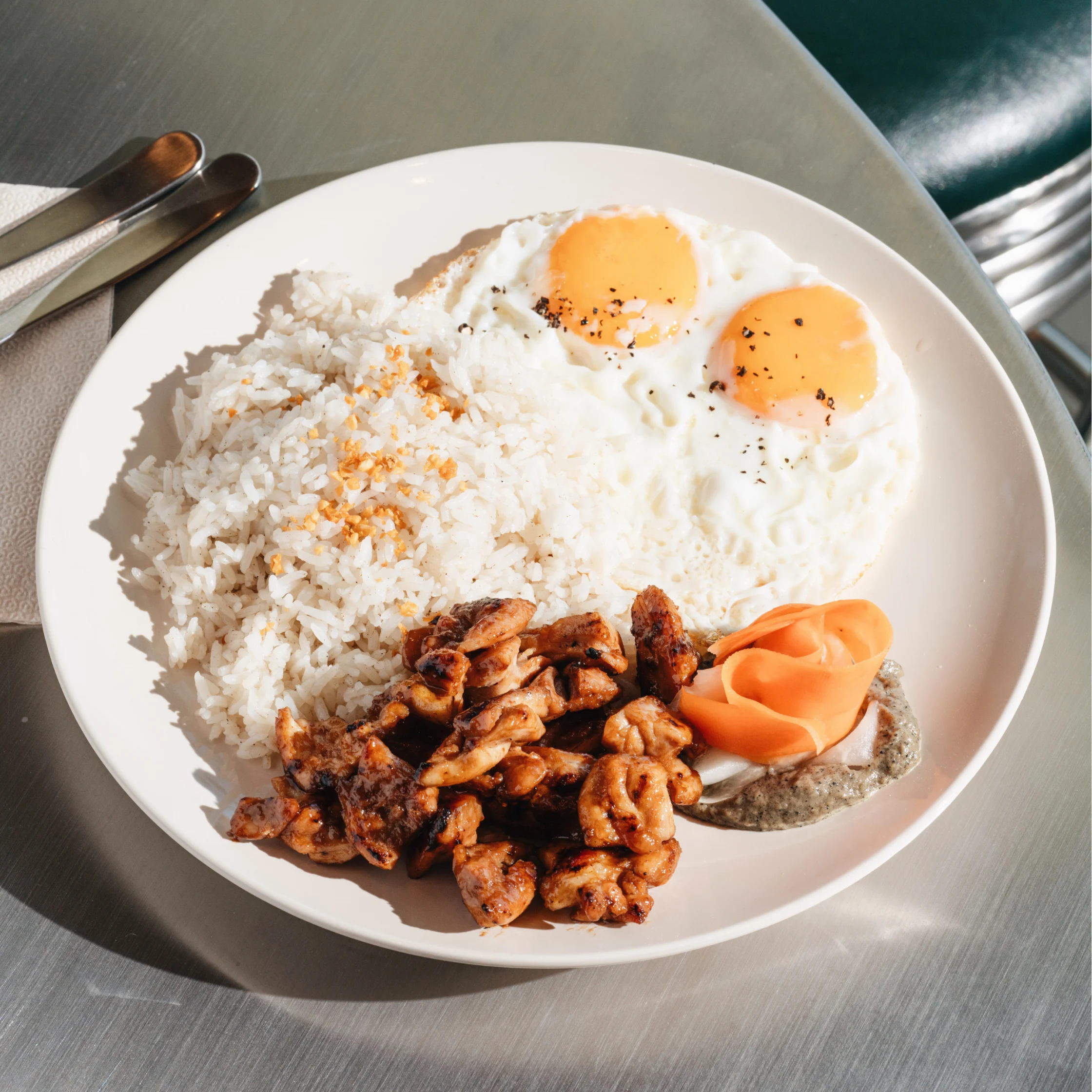 Savory meal at Hometown Cafe with garlic rice, grilled chicken, sunny-side-up eggs, pickled vegetables, and dipping sauce.