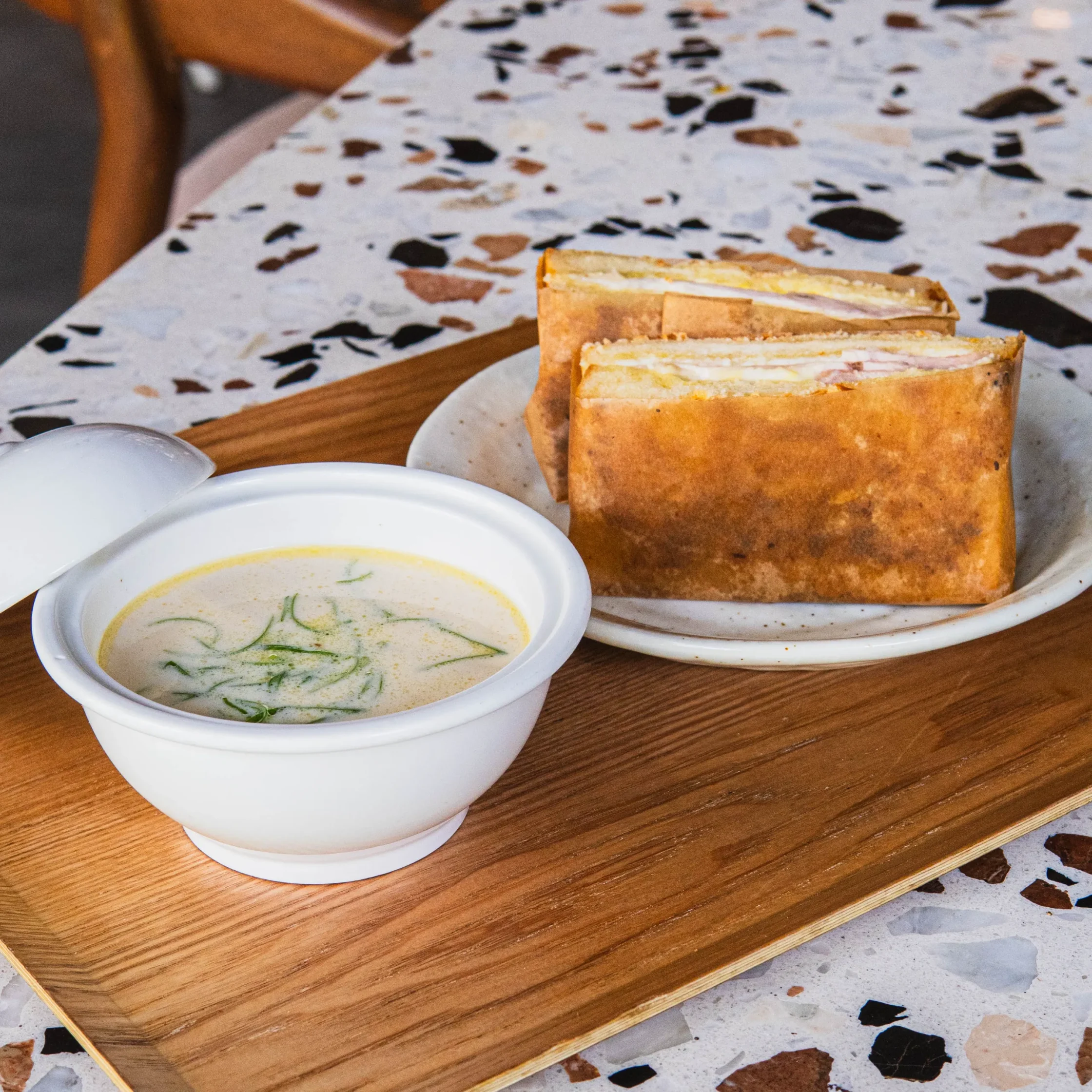 Toasted croque monsieur sandwich cut in halves and served with a bowl of creamy soup topped with shredded herbs.