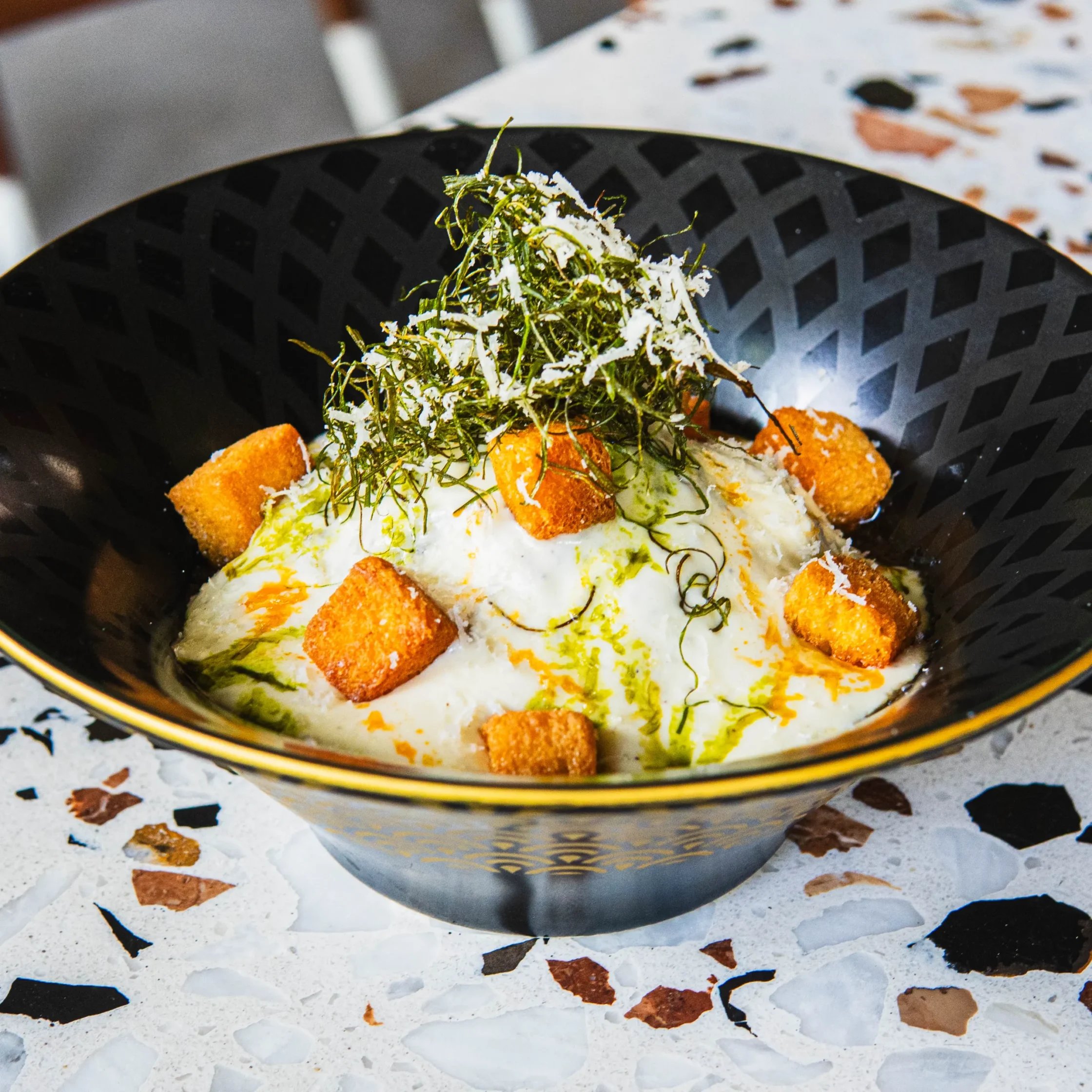 Bowl of creamy French onion maze soba noodles topped with crispy croutons, shredded seaweed, grated cheese, and herb oil.