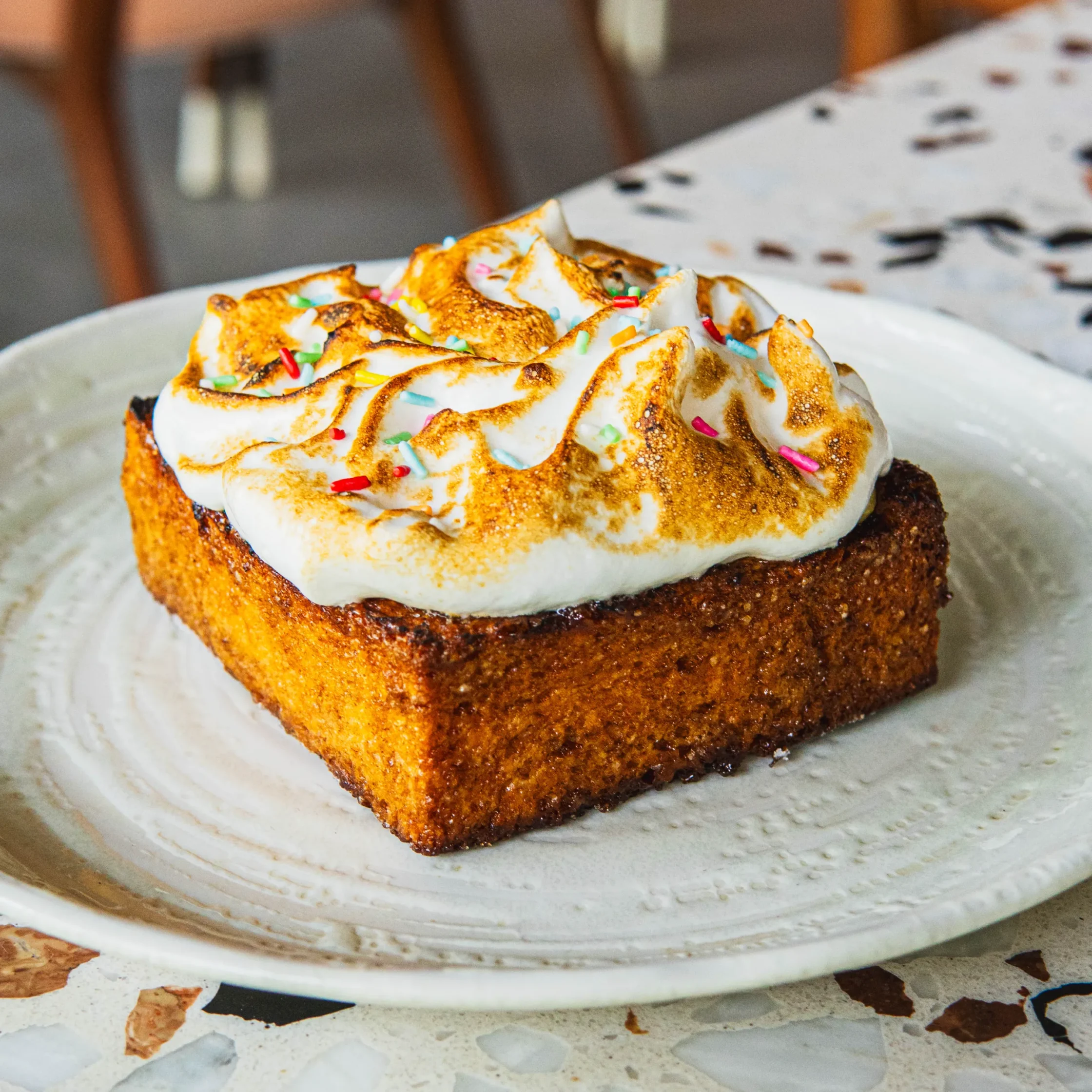 Thick slice of yuzu French toast topped with toasted meringue and colorful sprinkles on a ceramic plate.