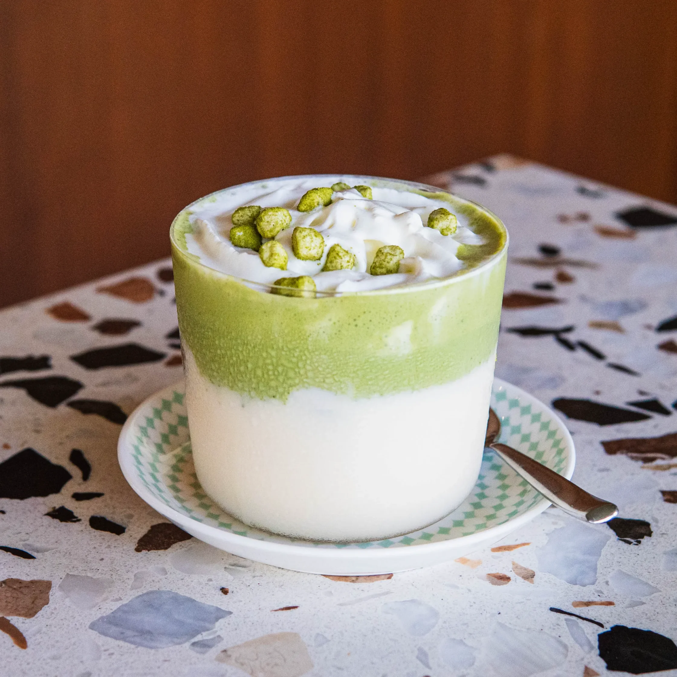 Iced Yakult matcha drink layered with milk and matcha, topped with whipped cream and matcha cereal puffs.