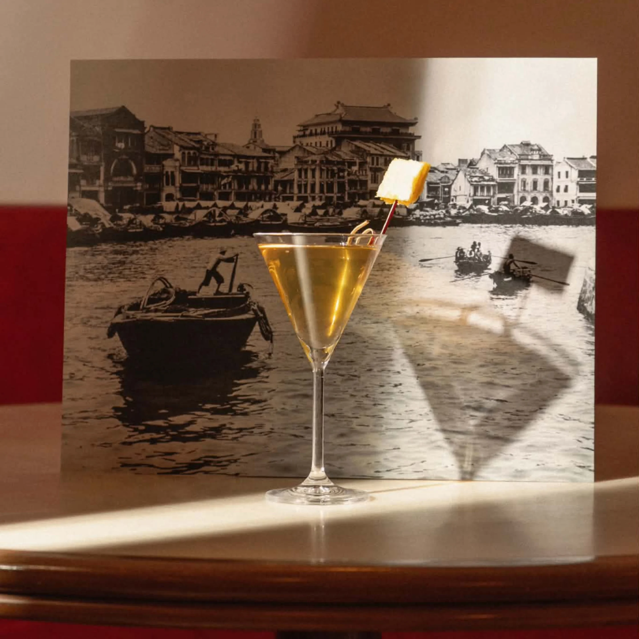 A cocktail sits in front of a vintage waterfront photograph, evoking the cultural exchange behind the Kinsman x Lazy Suzy menu, where Hong Kong and Manila influences meet in a single glass.