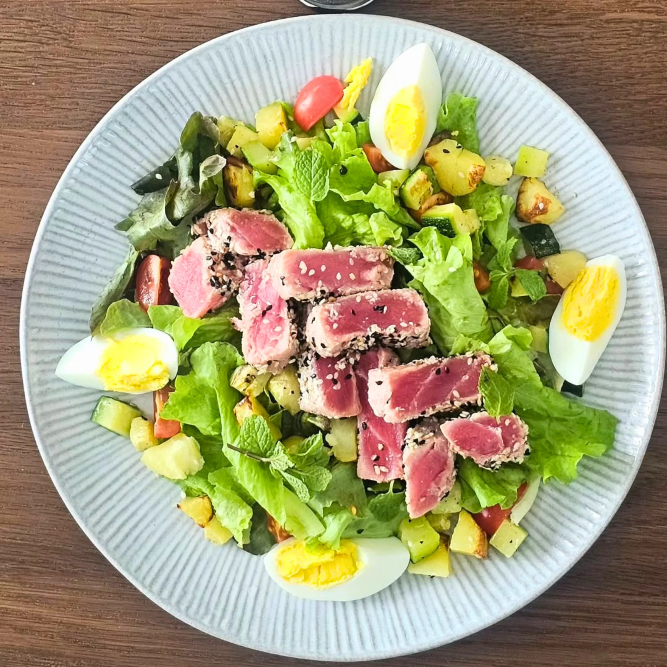 A fresh salad prepared by Private Chef Geron Altamirano, featuring seared tuna, mixed greens, vegetables, and hard-boiled eggs on a gray ceramic plate.