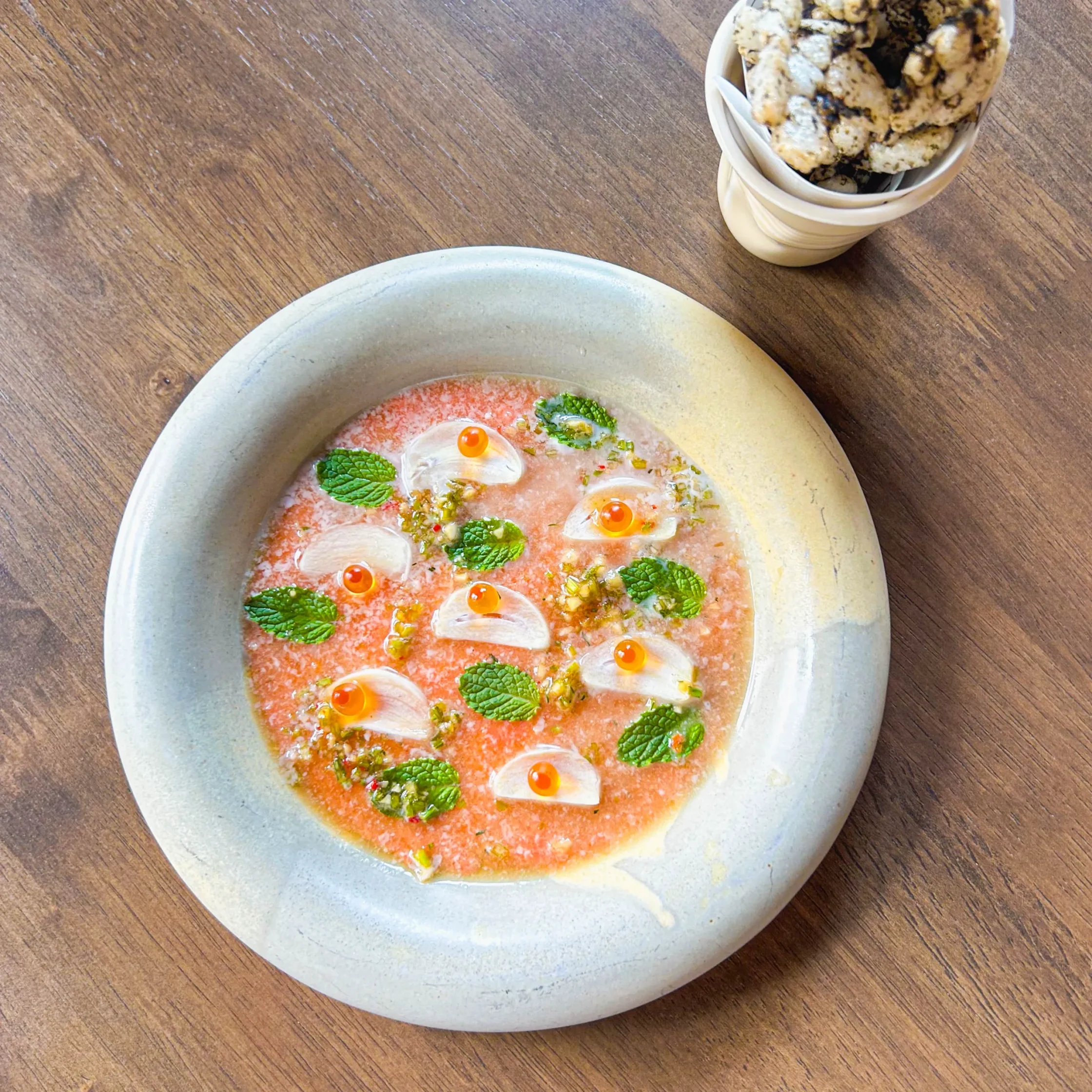 Chilled salmon dish served in a pink citrus-based sauce, garnished with mint leaves, thinly sliced shallots, herb dressing, and bright orange roe pearls.
