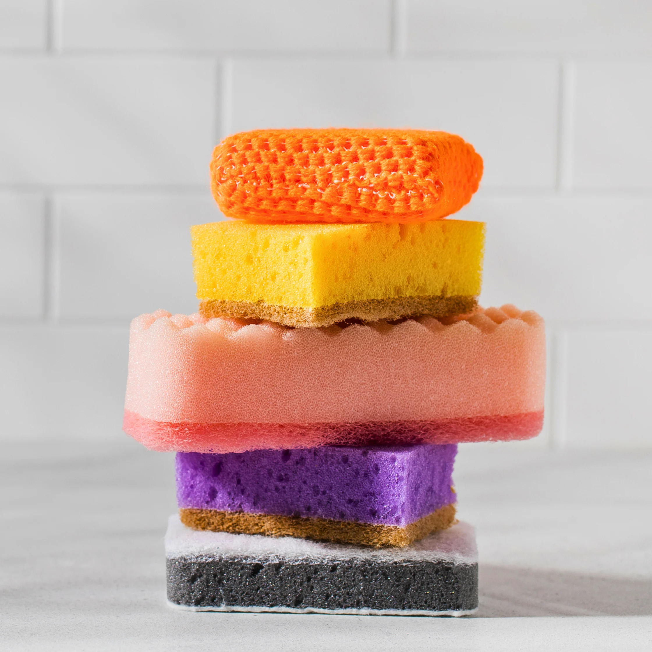 Several different cleaning sponges stacked on top of one another against a tiled background.