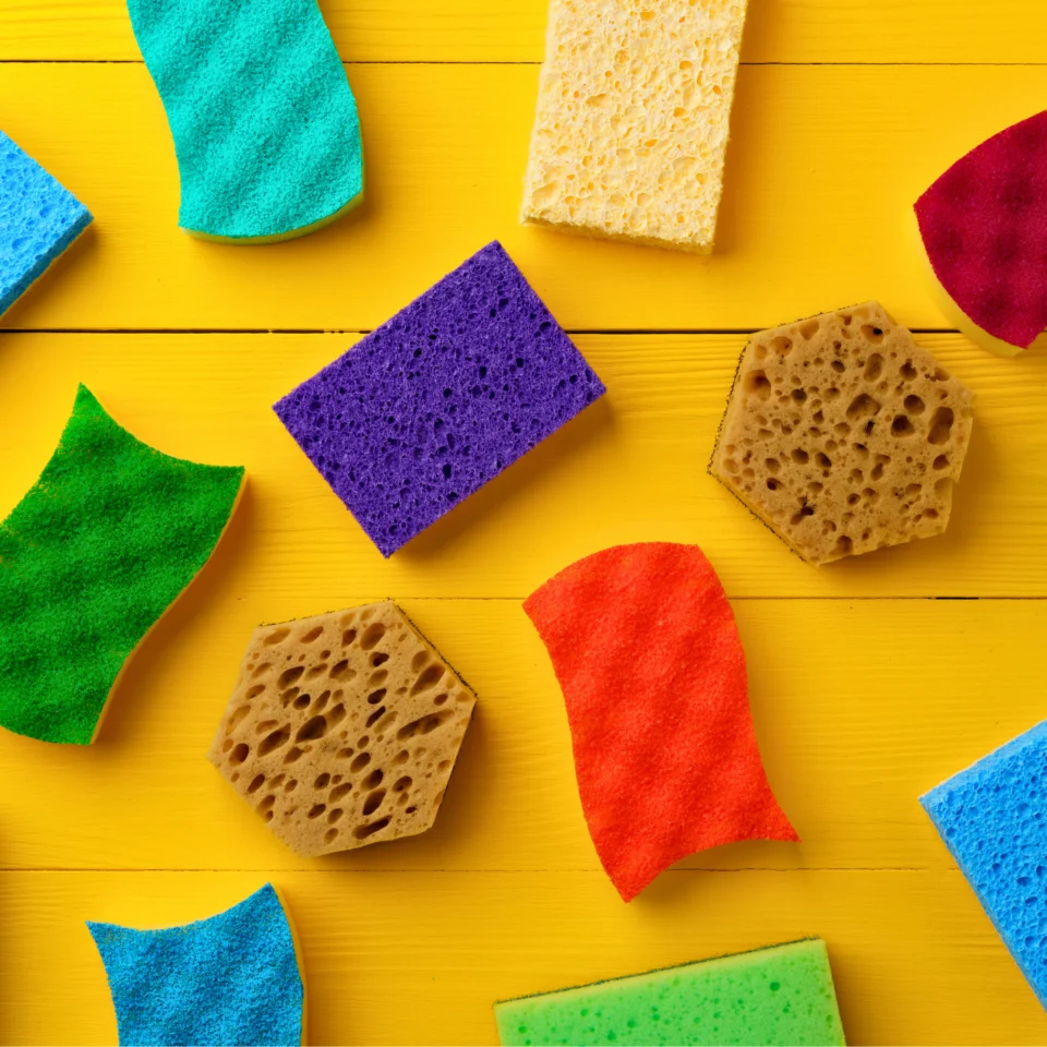 Colorful assortment of household sponges arranged on a bright yellow surface.