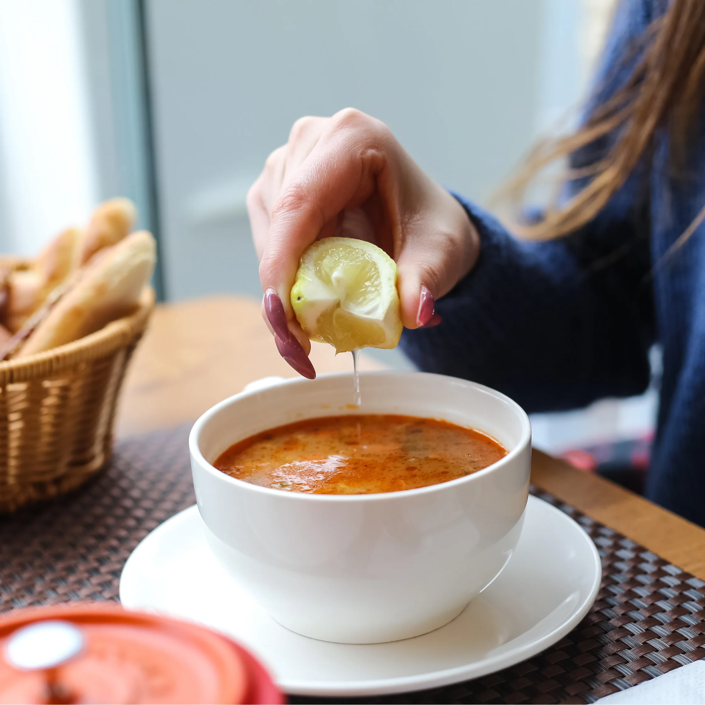 lemon juice being added to a bowl of bright orange soup for add tang and less saltiness