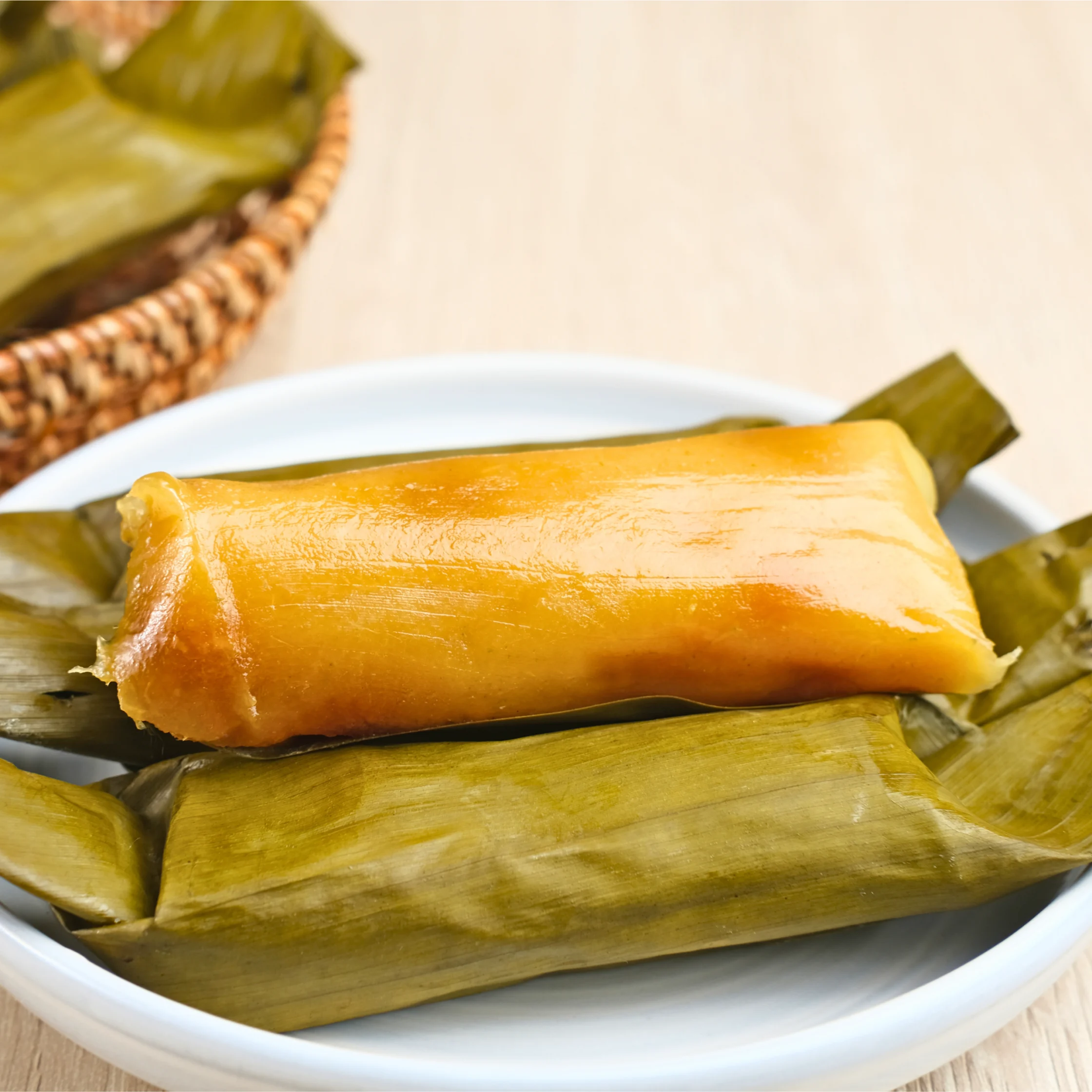 Filipino suman rice cake wrapped in banana leaves, with one unwrapped piece displayed on a plate.