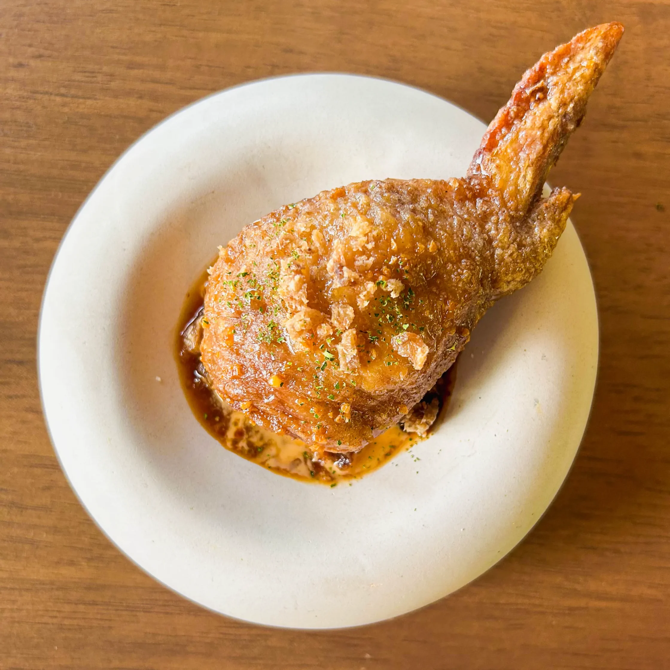 Crispy fried chicken leg with a golden-brown crust, served over a savory sauce and sprinkled with crunchy fried garlic pieces.