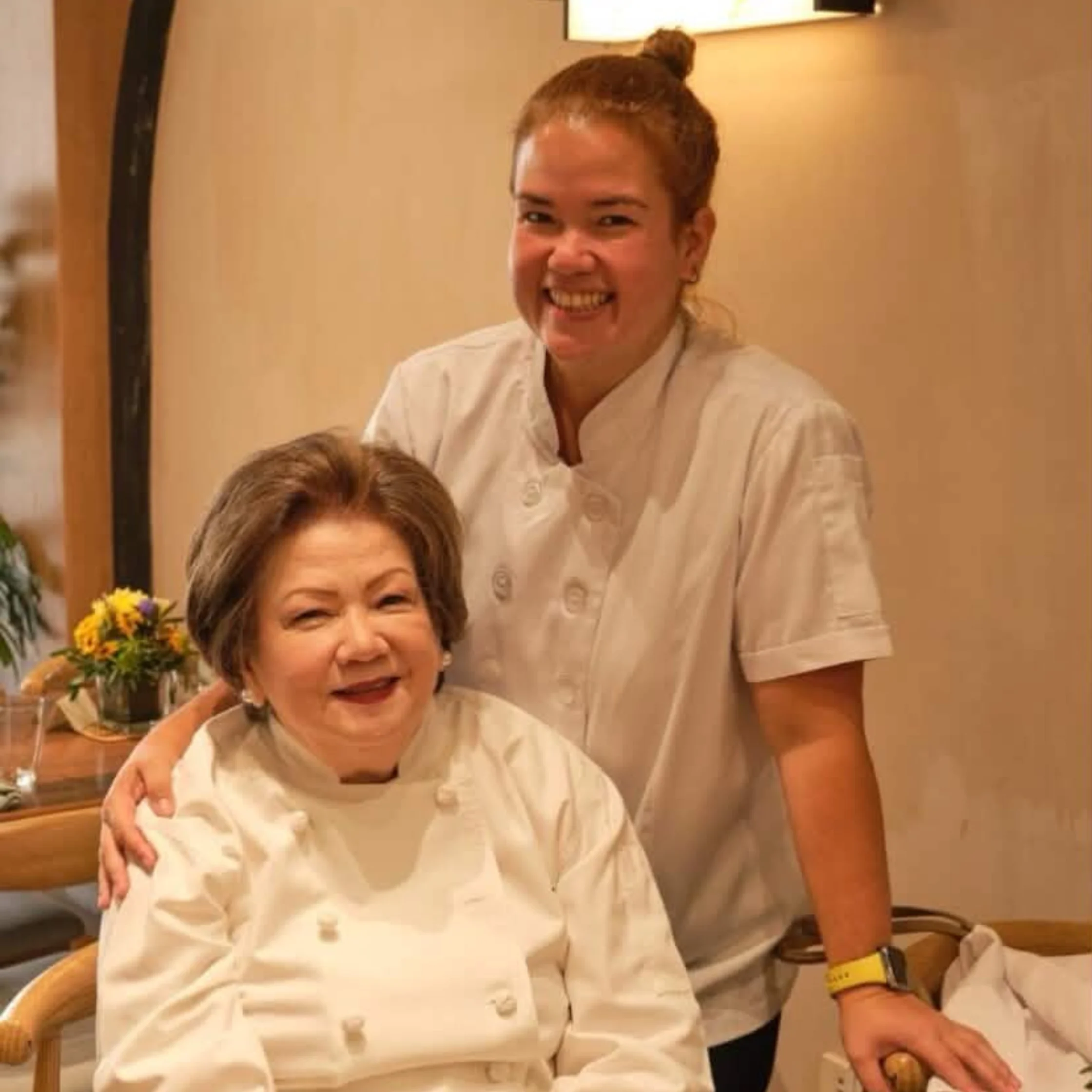 Tina Legarda and her mom, Bettina Legarda, wearing chef jackets and posing together indoors.