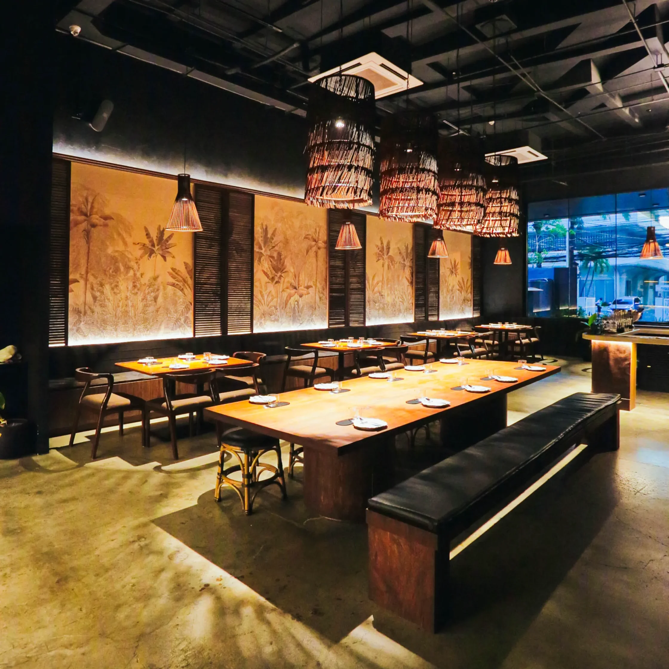 The dining area at Toma Toma features communal wooden tables, woven pendant lights, and decorative panels inspired by Philippine landscapes and craftsmanship.