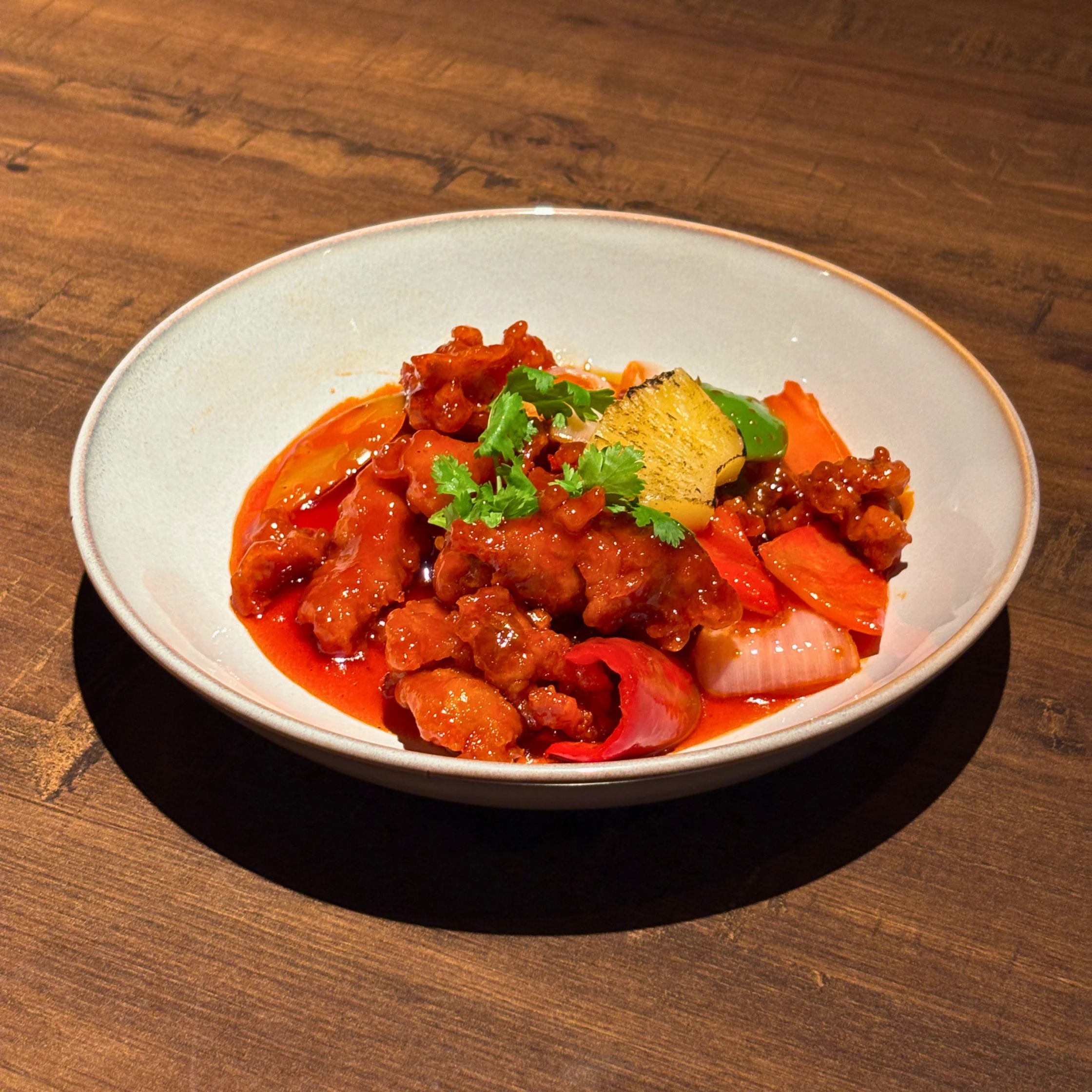 Sweet and sour pork in a bright red sauce with pineapple, bell peppers, and onions, garnished with fresh cilantro.
