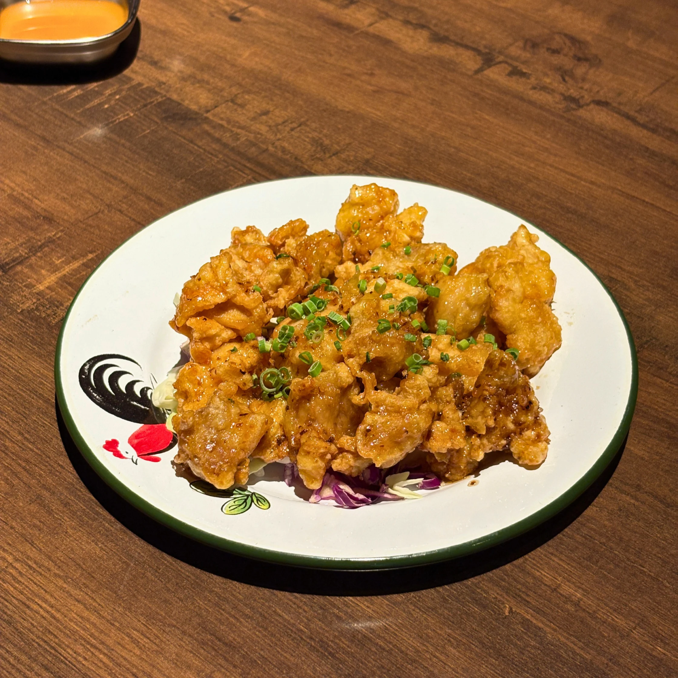 Plate of crispy truffle honey chicken pieces topped with chopped green onions and served over shredded cabbage.