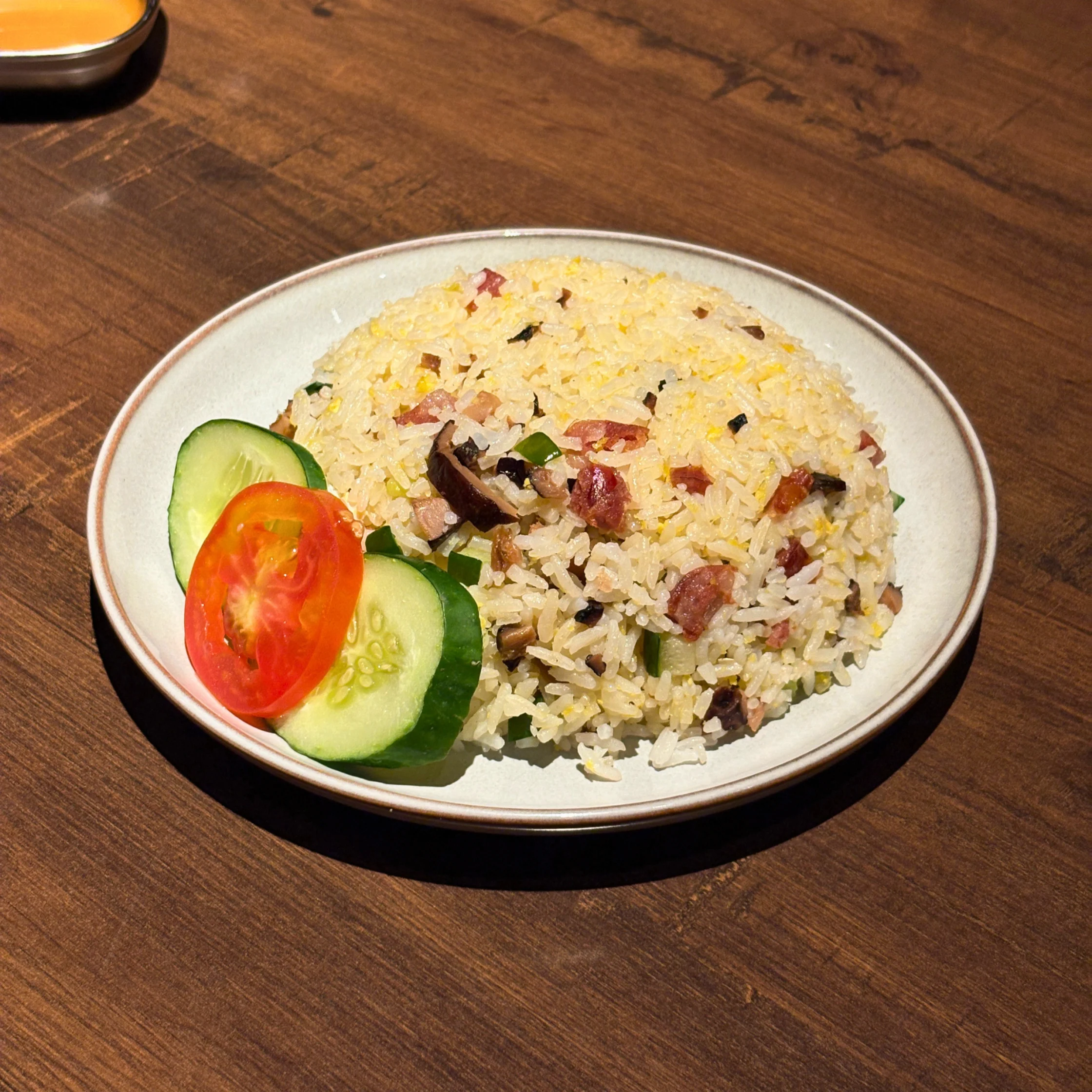 Plate of Wong Chow fried rice with bits of barbecue pork, egg, and vegetables, served with cucumber and tomato slices on the side.