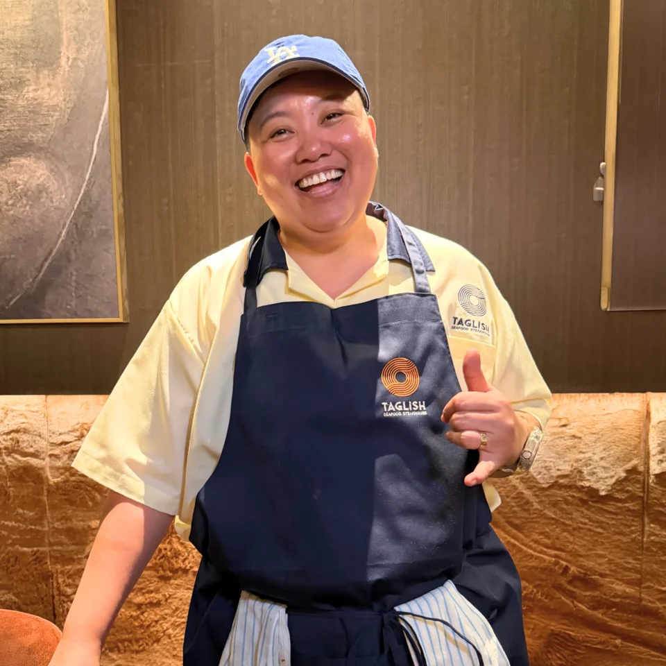 a chef standing in font of the camera smiling wearing a blue cap and blue apron